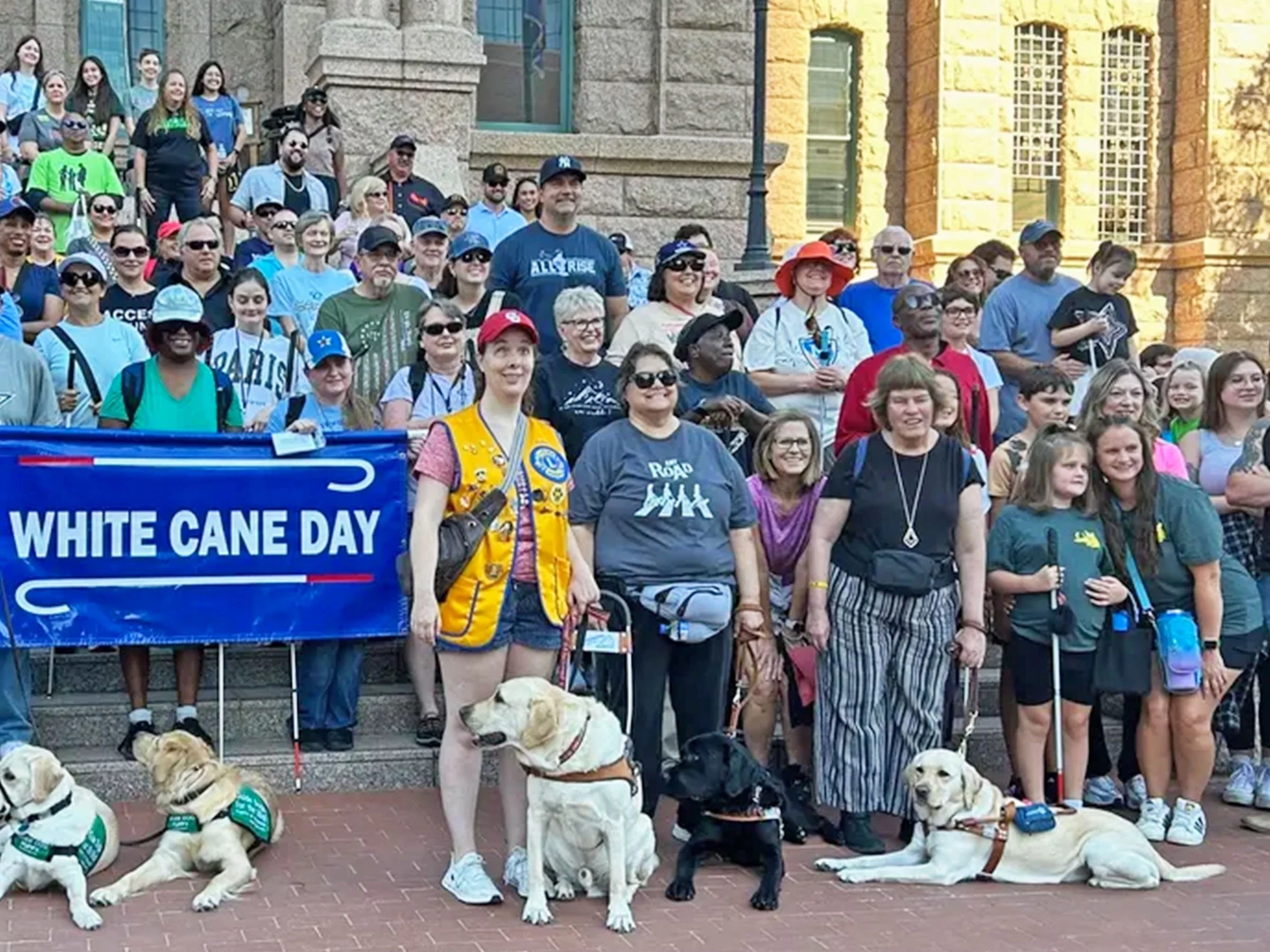 A large group of blind individuals, surrounded by seeing eye dogs and non-blind supporters, stand in the Fort Worth square during White Cane Day 25. 