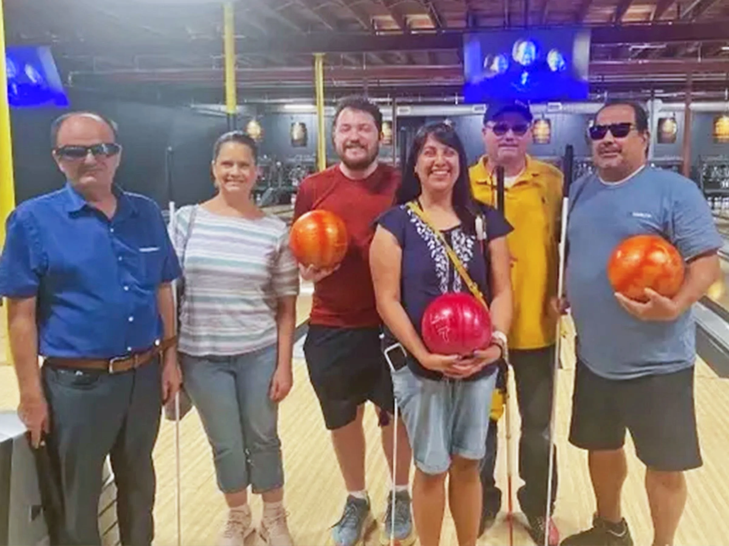 Six Fort Worth residents hold bowling balls and smile for the camera, after competing in the Visually Impaired and Blind Bowling Challenge in 2023.