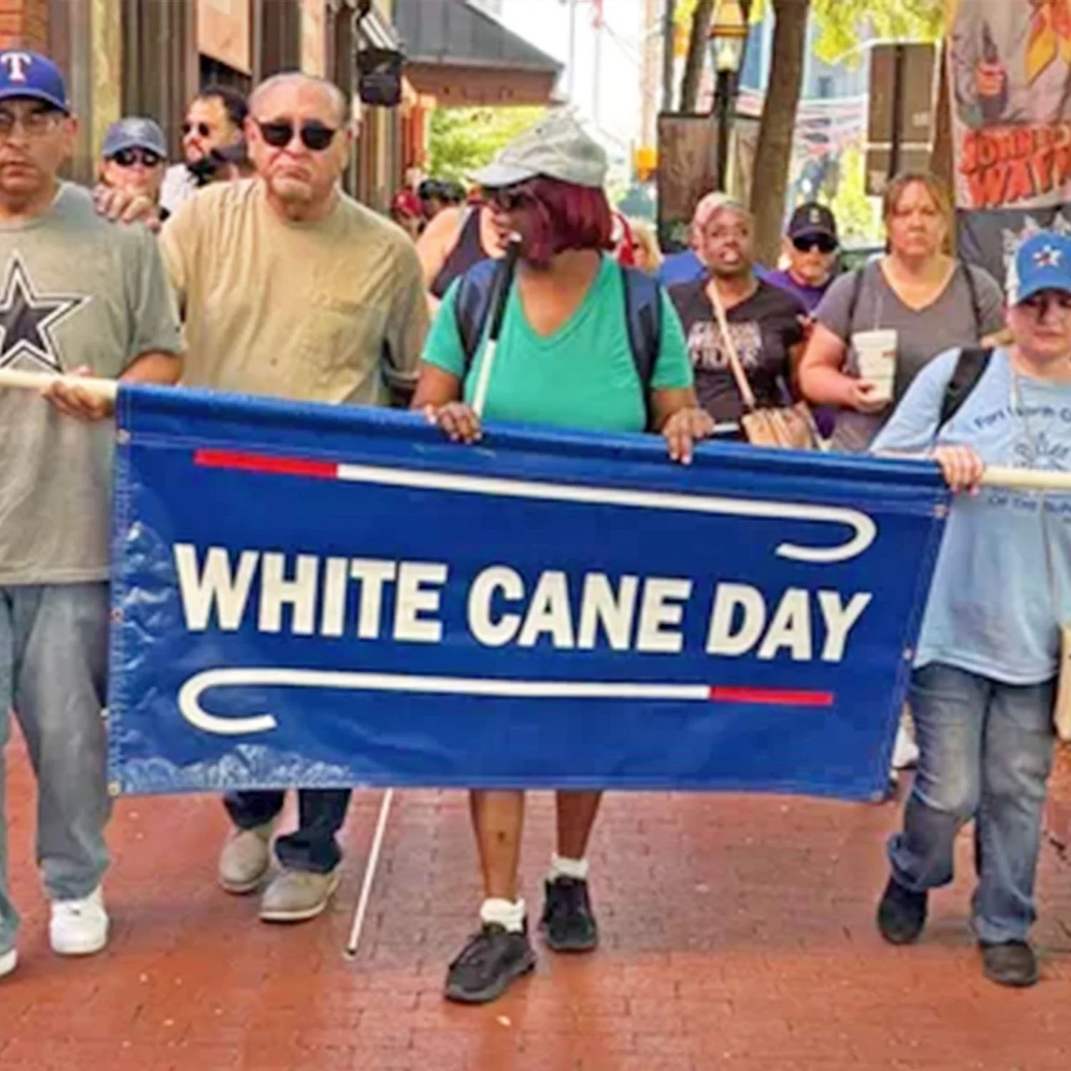 A group of proud visually impaired and blind individuals march for White Cane Day, as they hold up their colorful blue White Cane Day sign.