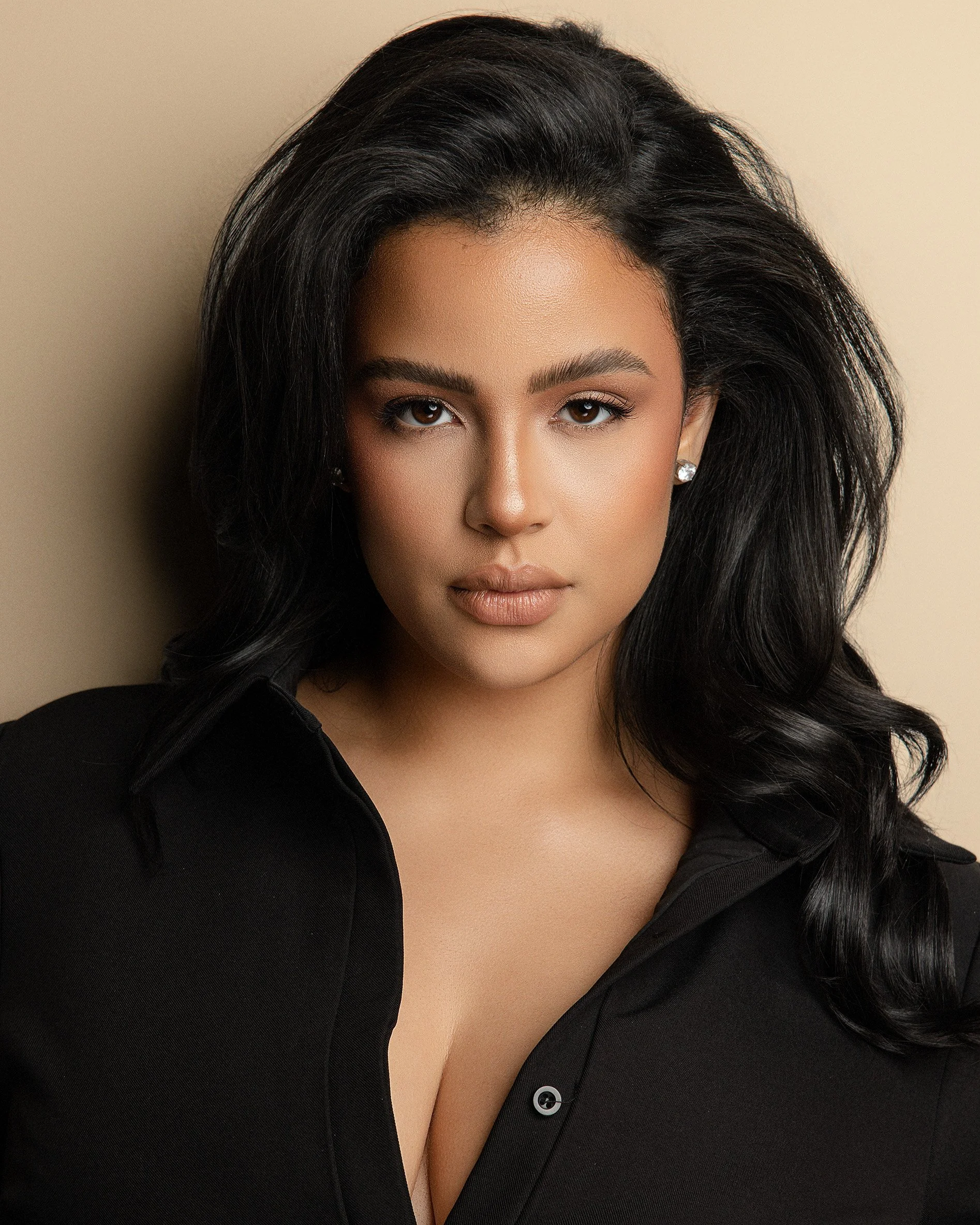 A woman with dark hair, wearing a black shirt, looking directly at the camera against a light beige background.