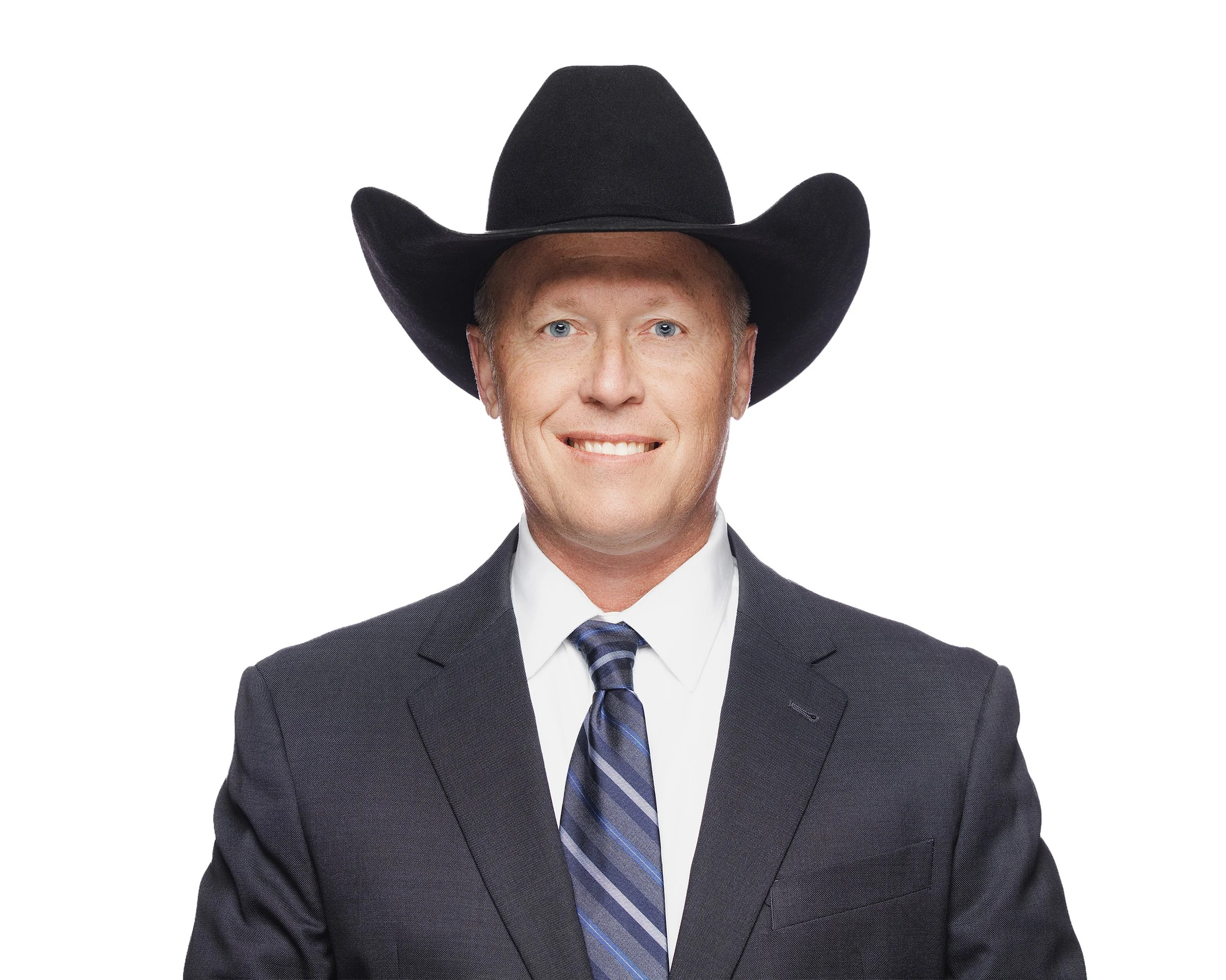 A man smiling wearing a dark suit, white shirt, blue patterned tie, and a large black cowboy hat.