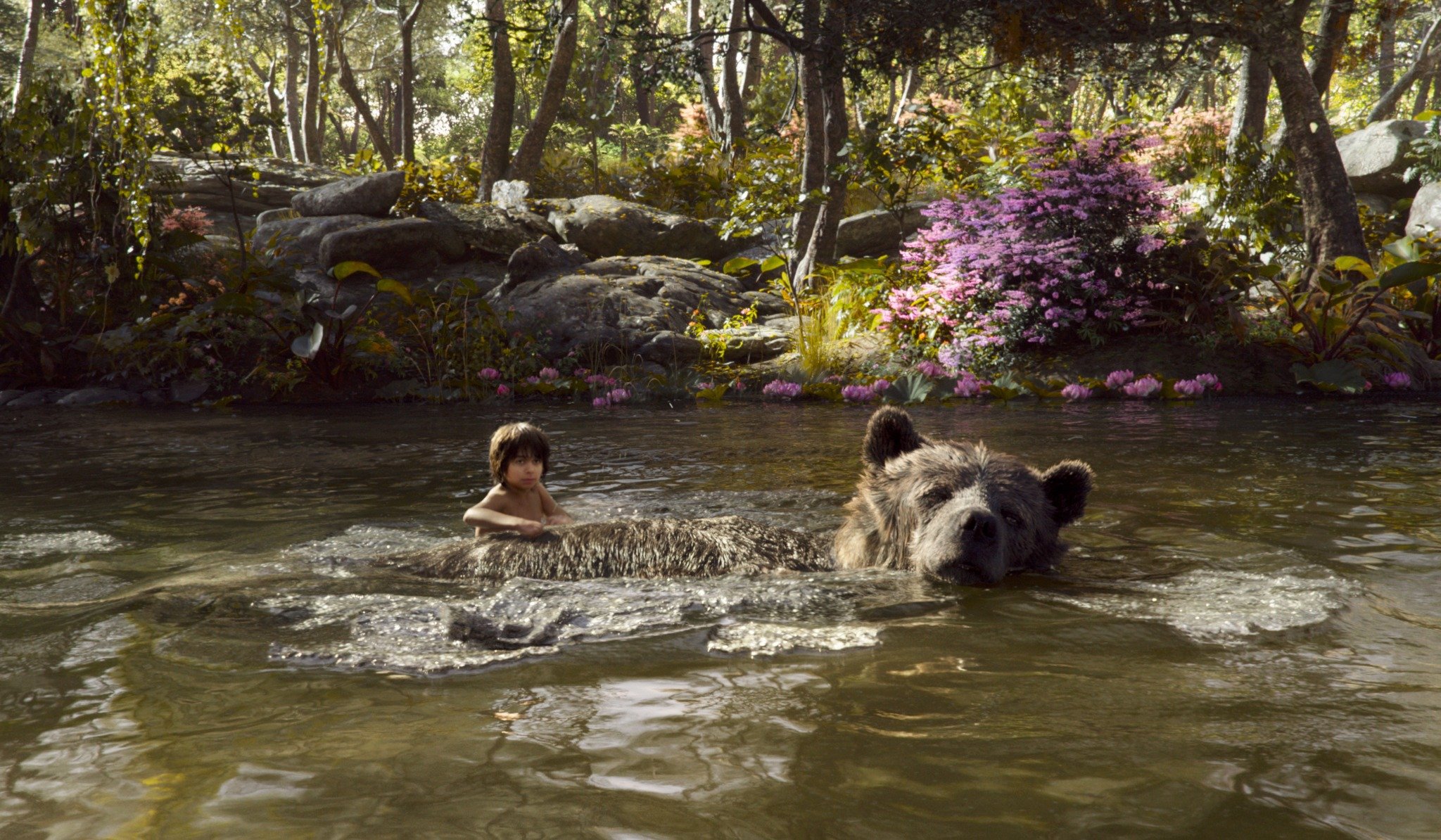 A young boy swimming in a river with a large bear in the water, surrounded by trees and pink flowers.