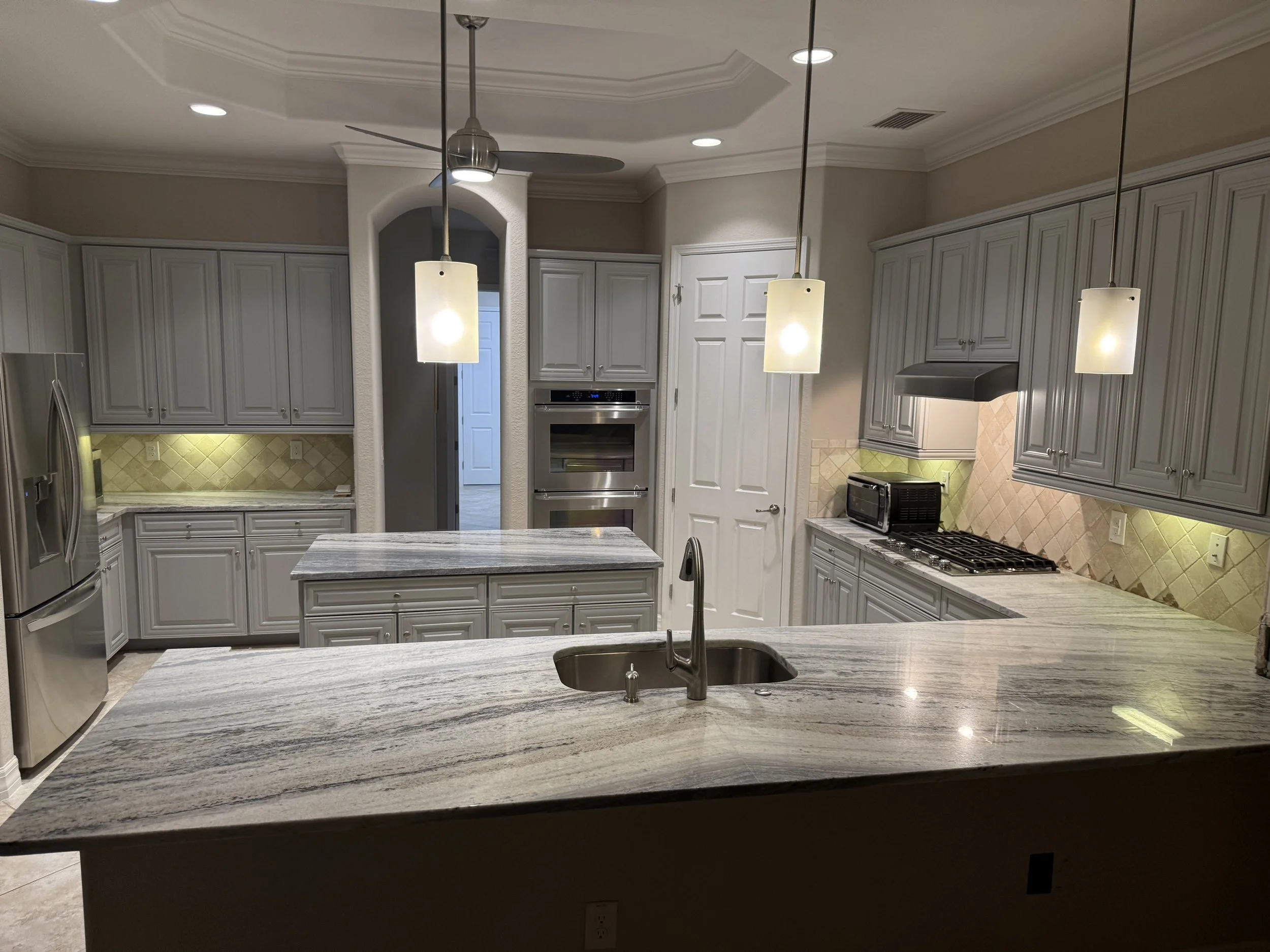 Modern kitchen with gray cabinets, granite countertops, stainless steel appliances, and pendant lighting.