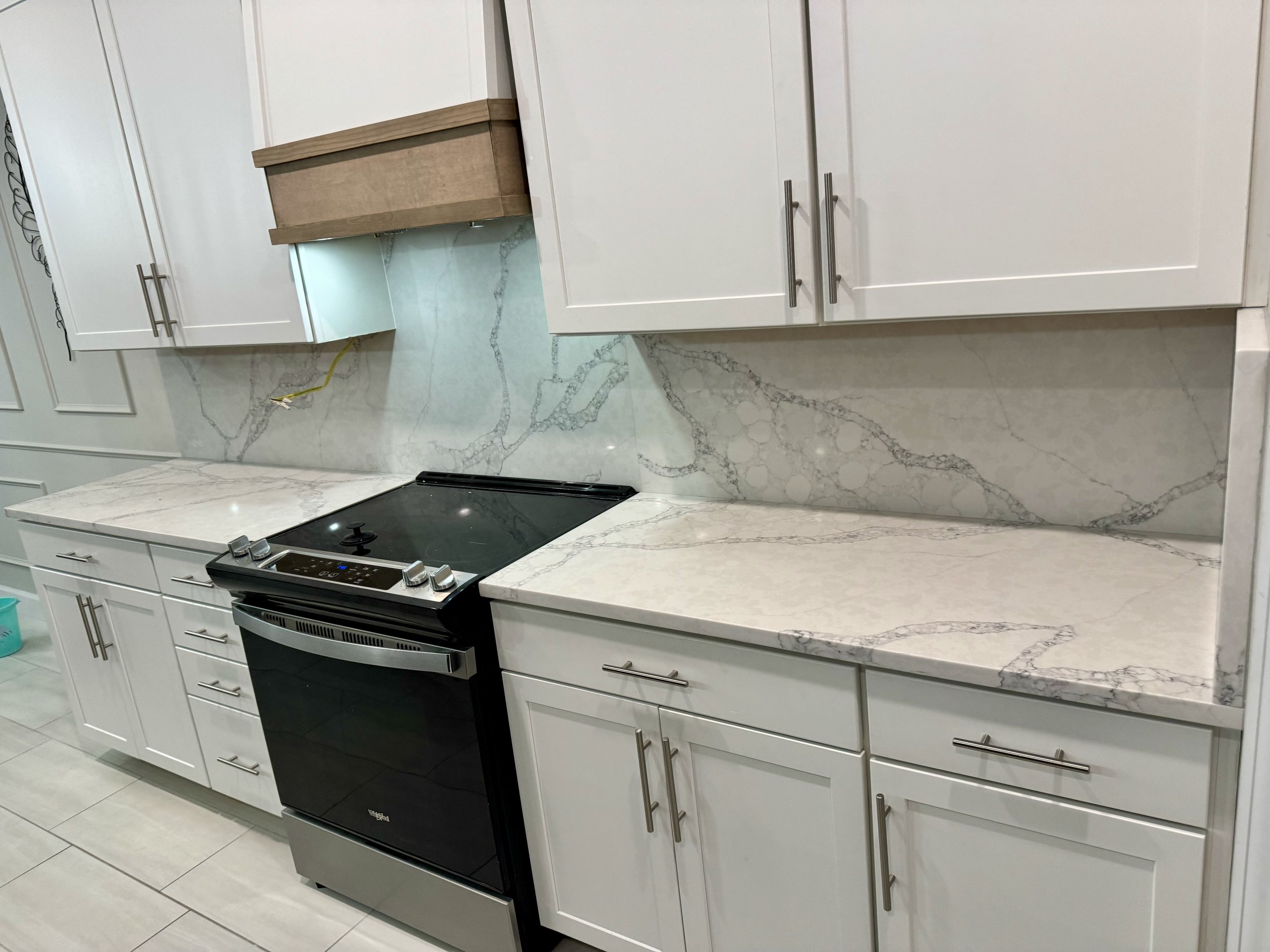 Kitchen with white cabinets, marble countertops, a black stove, and a marble backsplash.