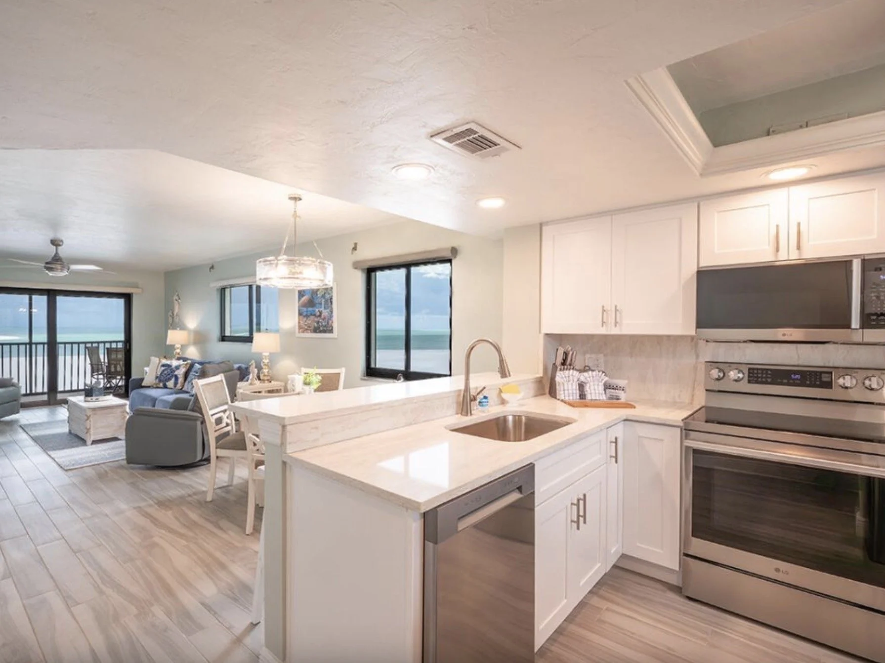 Open-concept living room and kitchen with ocean view, white cabinetry, stainless steel appliances, and light-colored wood flooring.