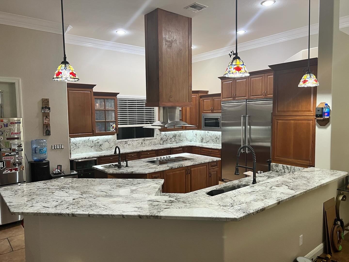 Modern kitchen with wooden cabinets, granite countertops, stainless steel appliances, and three stained glass pendant lights.
