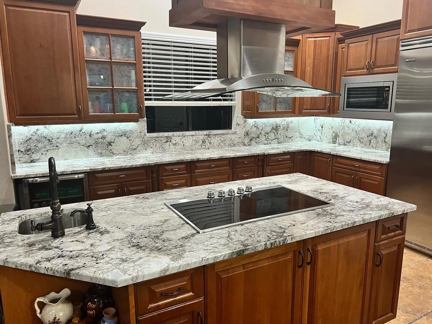 A kitchen with wooden cabinets, granite countertops, a stove, a sink, a microwave, and a stainless steel refrigerator.
