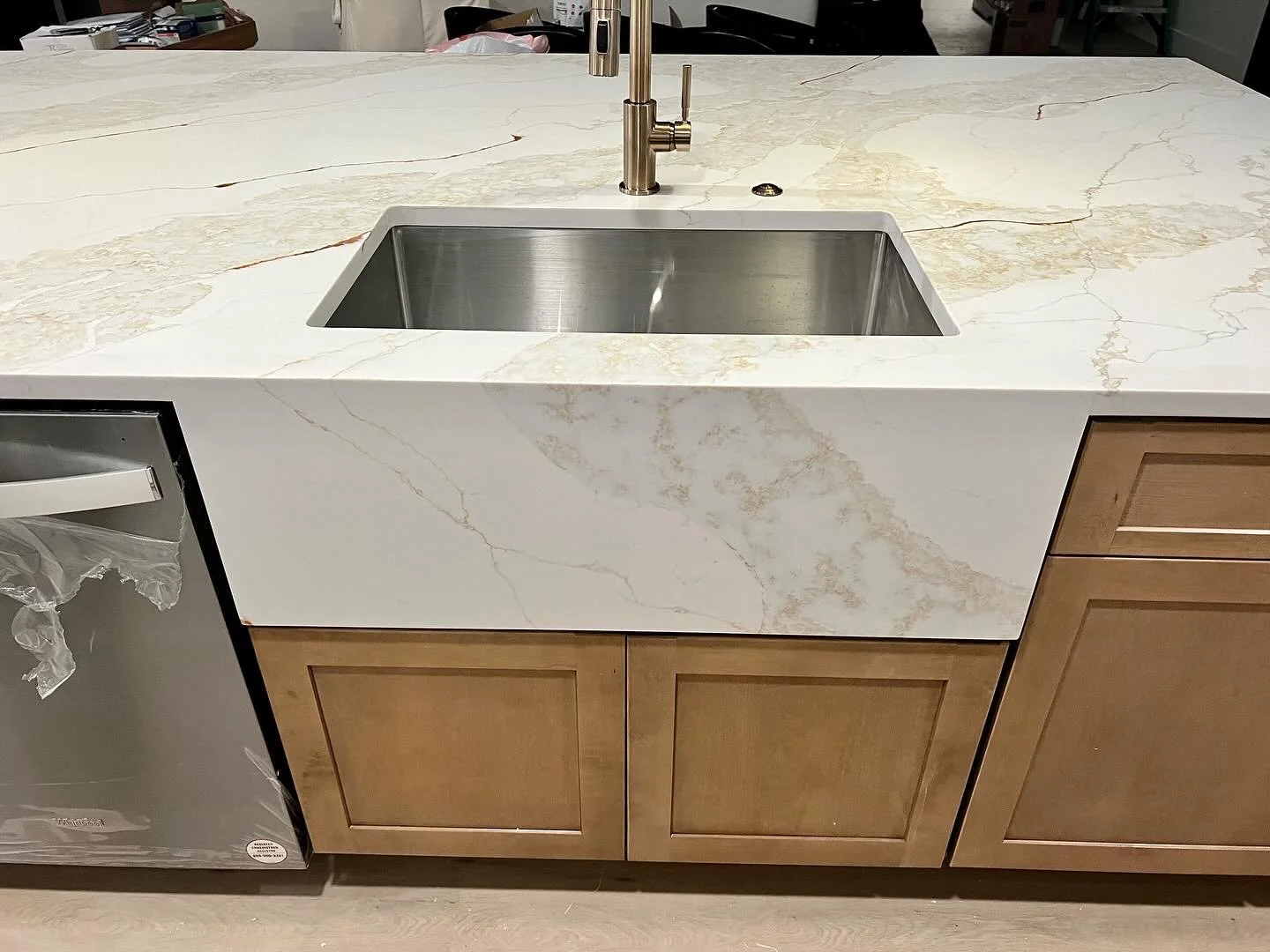 Kitchen island with a white marble countertop and a built-in stainless steel sink, with wooden cabinets below.