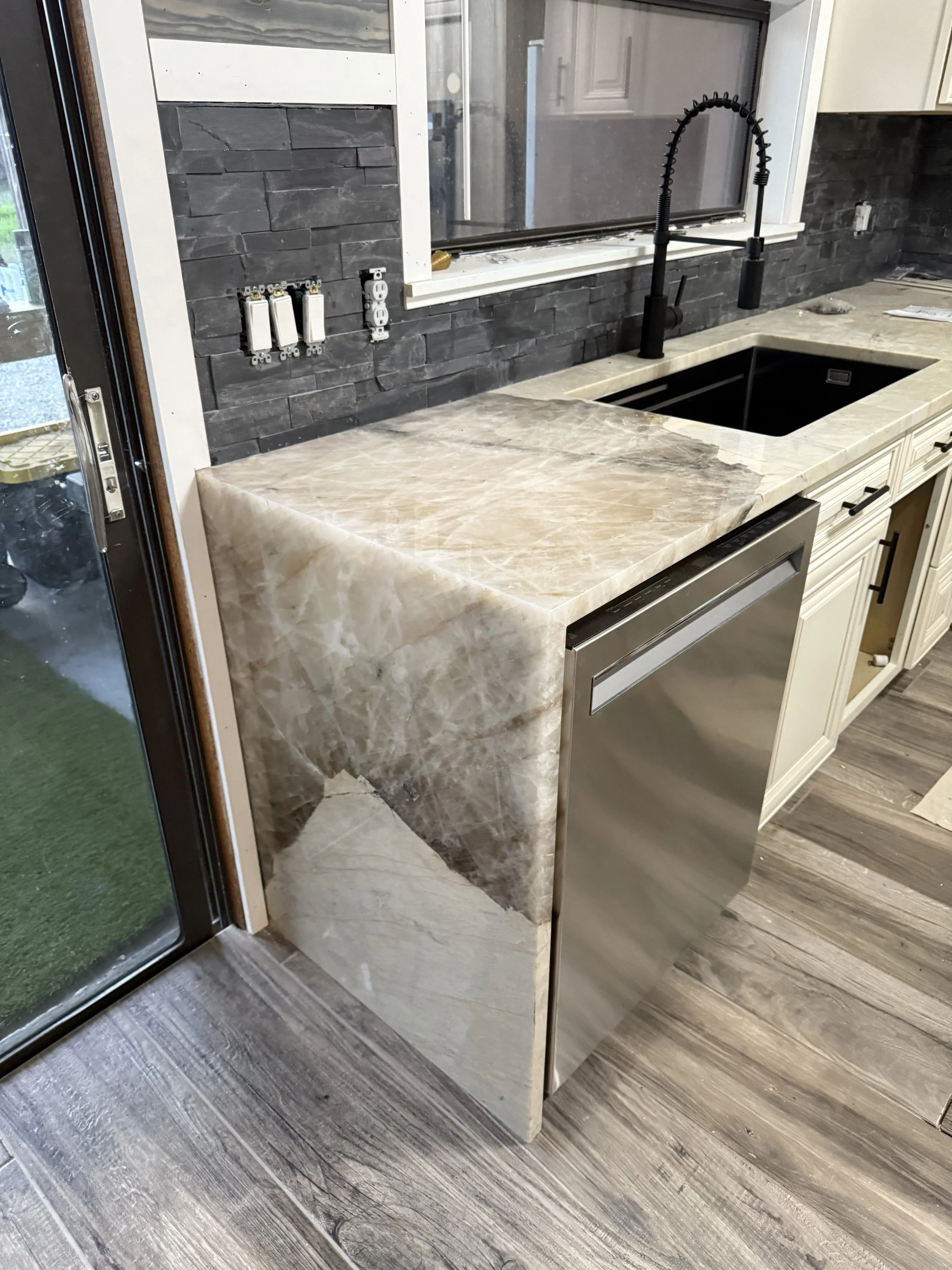 Modern kitchen with marble countertop, black sink, black faucet, white cabinetry, dark stone backsplash, and visible triple electrical outlets.