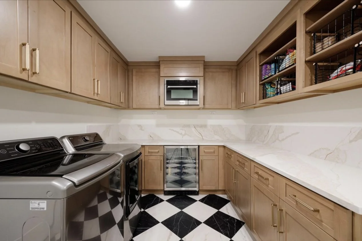 Laundry room with wooden cabinets, a washing machine, a wine cooler, microwave, and countertop with marble backsplash.