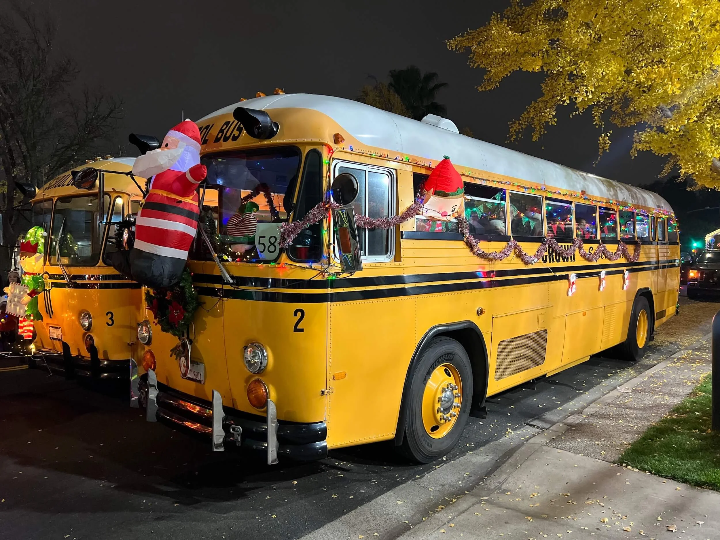 Decorated yellow school bus at night with Christmas and holiday decorations, including inflatable Santa, tinsel, lights, and festive ornaments.