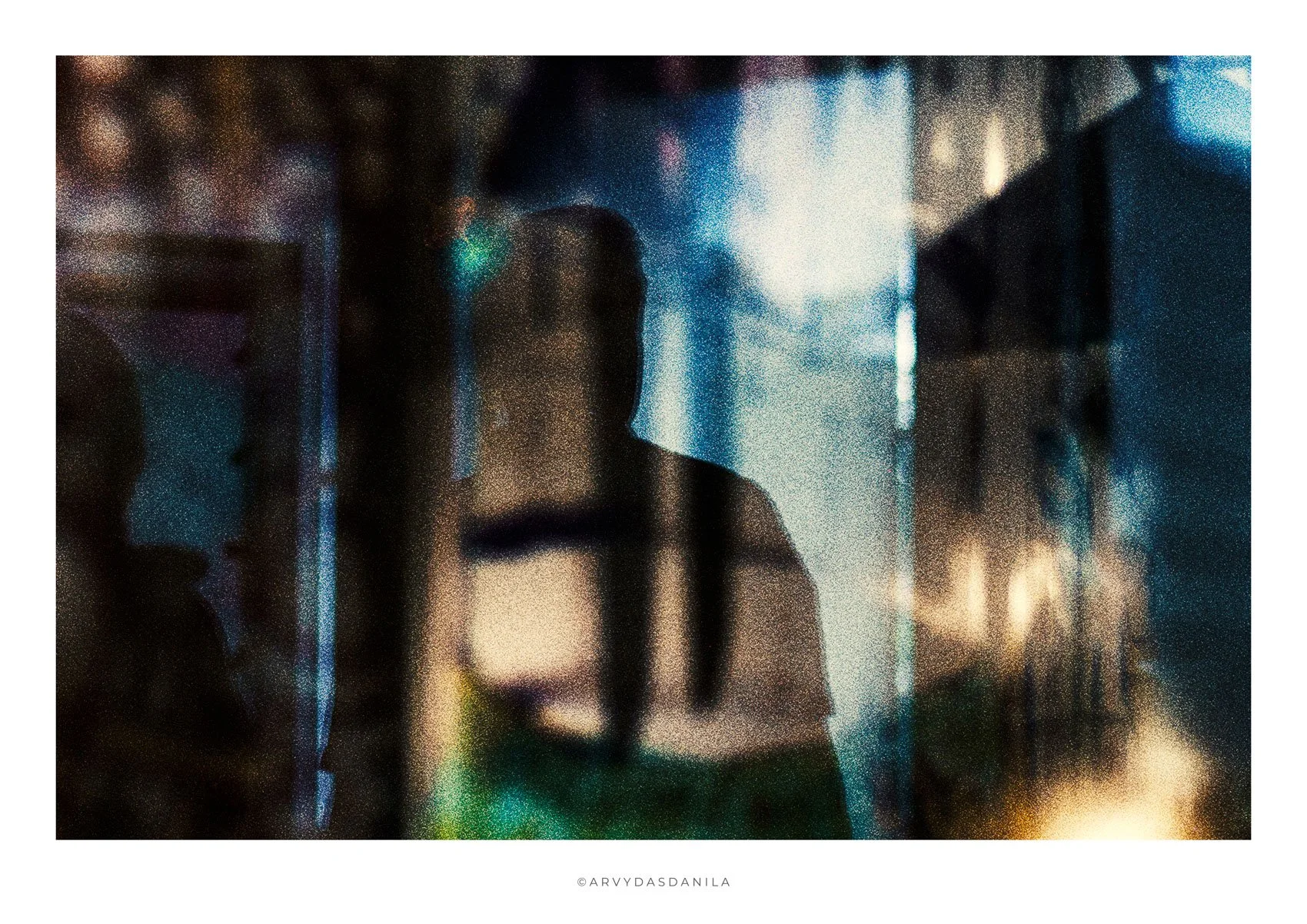 A blurry, pixelated photo of a woman standing in front of a glass window with industry-like structures and bright lights in the background. The photo has a grainy effect and faint reflections.