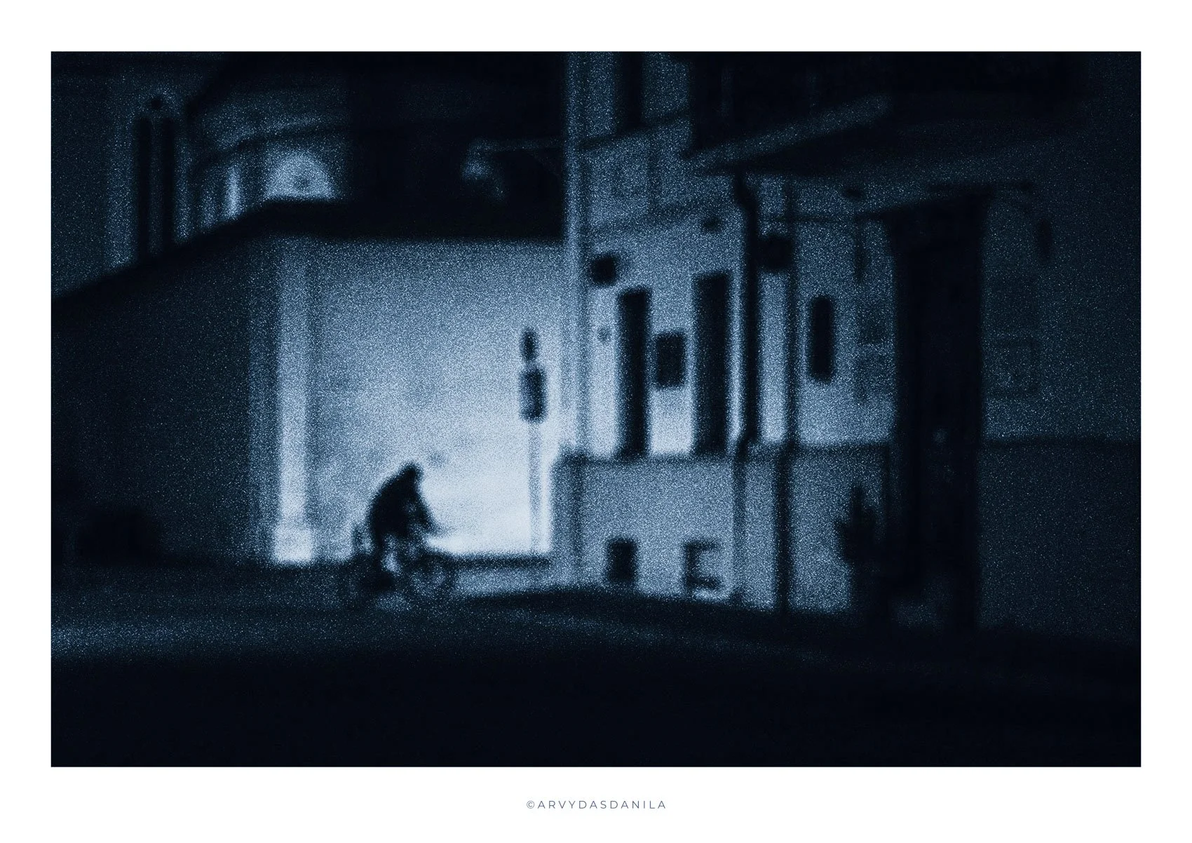A blue night gloomy shadows, image is out of focus showing the street scene a person on a bicycle unsettling Tarkovsky like visual poetry. Stunning impressive and standing out photograph.
