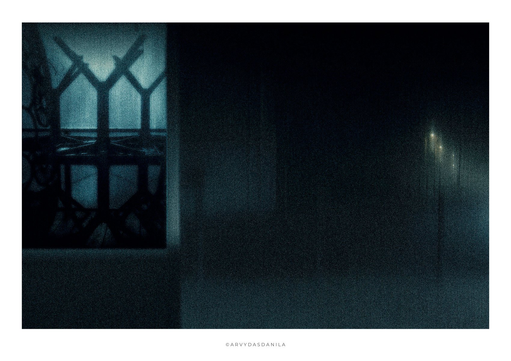 A dark, foggy scene shows a silhouette of a wrought-iron blue theme visual window to the space with sleeping chairs and tables depicting the end and beginning with row of distant streetlights fading into the fog on the right very sophisticated look