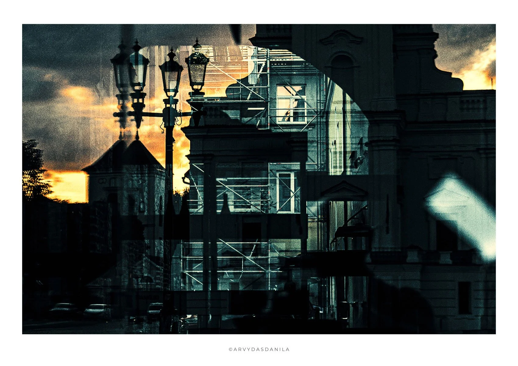 Sunset cityscape with scaffolding on buildings and street lamps, reflecting an urban scene at dusk.