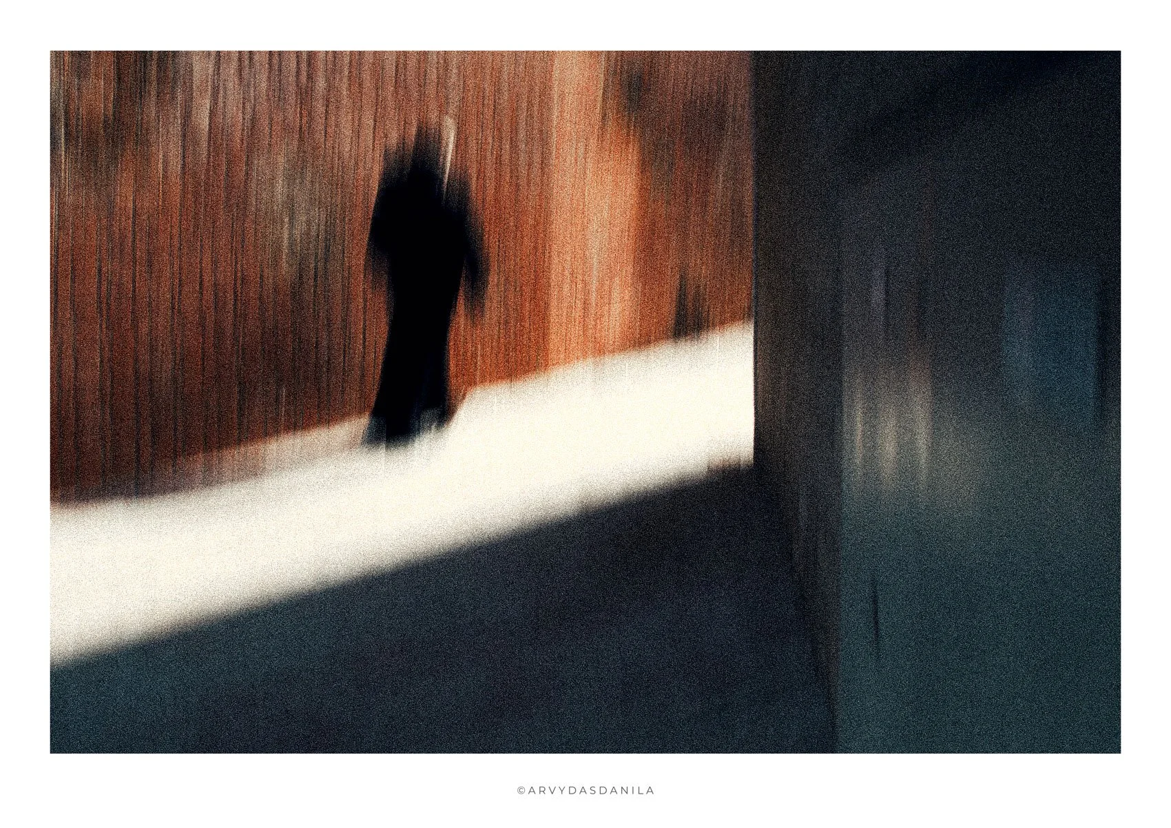A blurry silhouette of a person walking in a corridor with wooden walls and a light-colored floor.