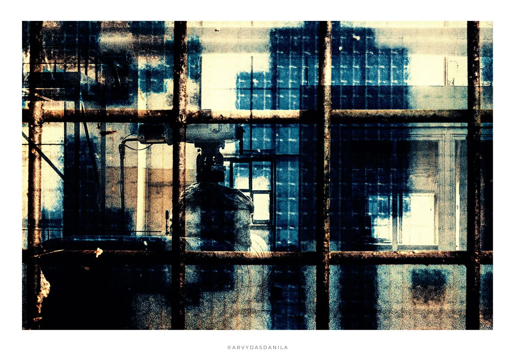 Industrial scene of metal pipes and machinery viewed through a dirty, rusted glass window with a grid pattern, giving a moody, gritty atmosphere.