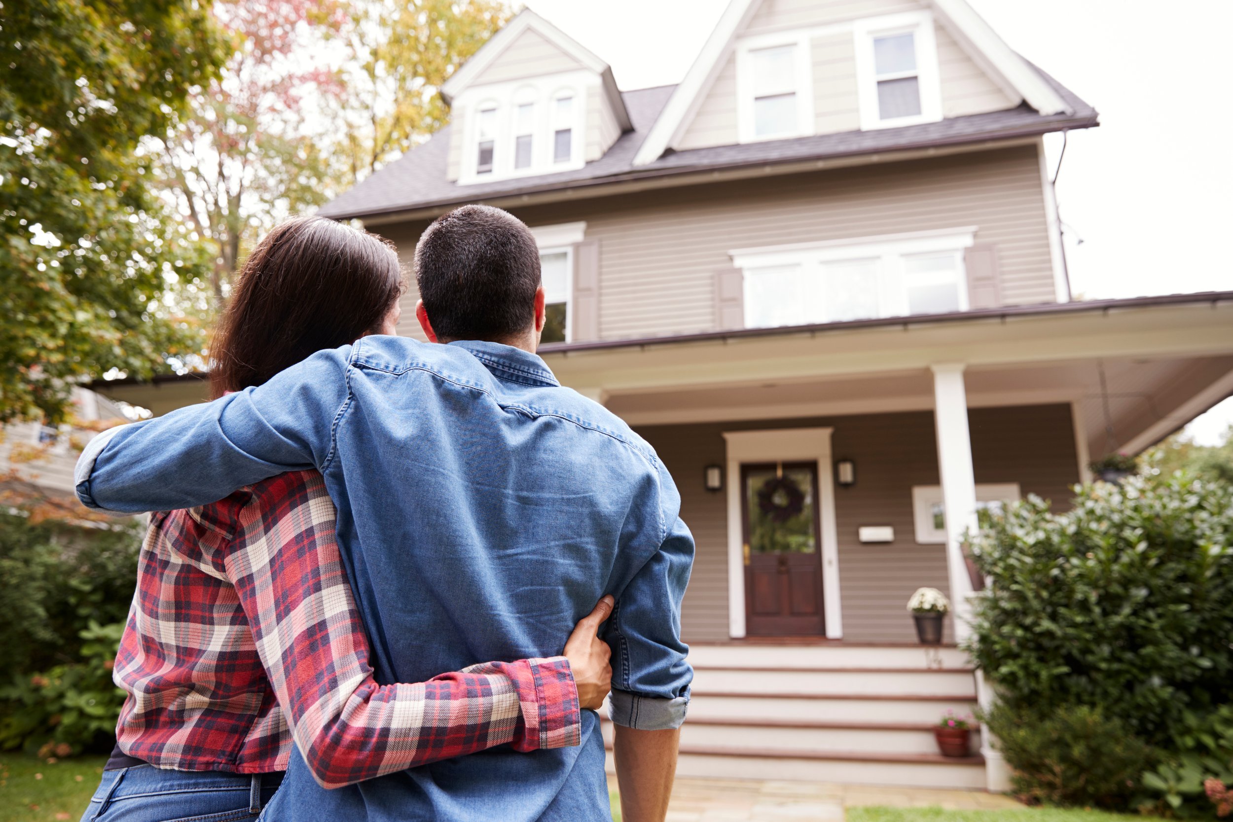 Couple standing in front of a house, embracing, with trees around, during daytime.