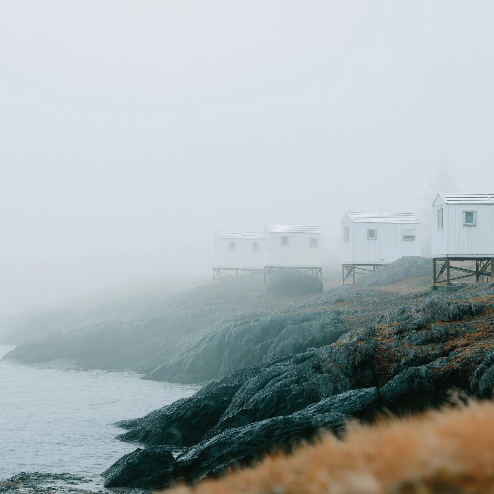 Overcast sky with white clouds and white houses on stilts overlooking the ocean, rocky shoreline in foreground