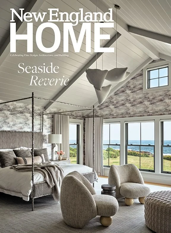 A bedroom with a view of the ocean through large windows, featuring a bed with neutral-colored bedding, modern chairs, a textured rug, and a uniquely designed ceiling with a white pendant light.