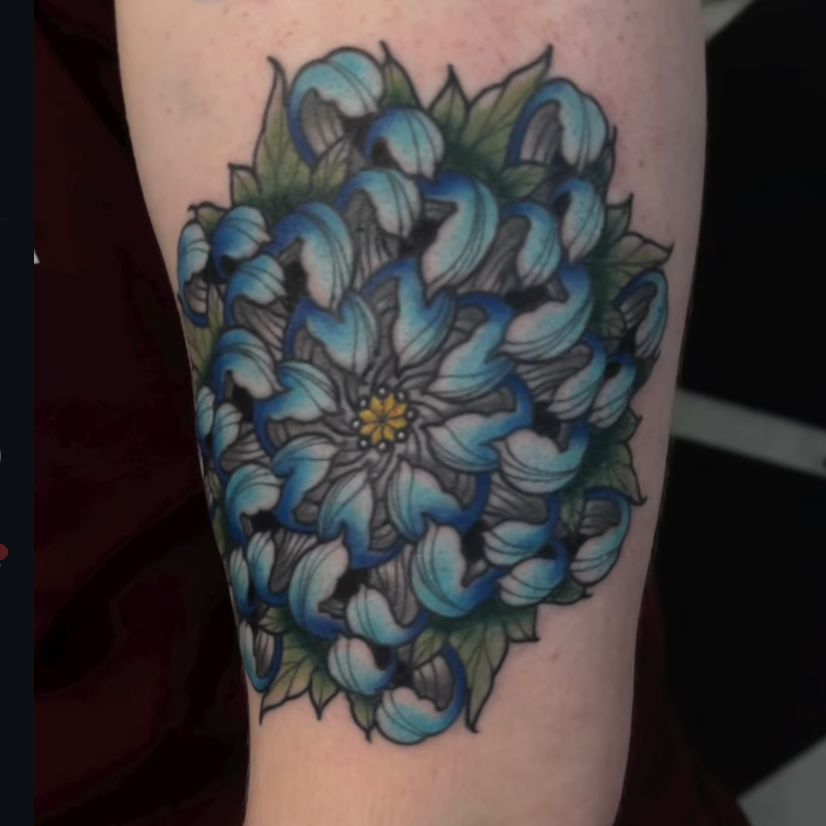 A tattoo of a blue and white flower with green leaves on skin.