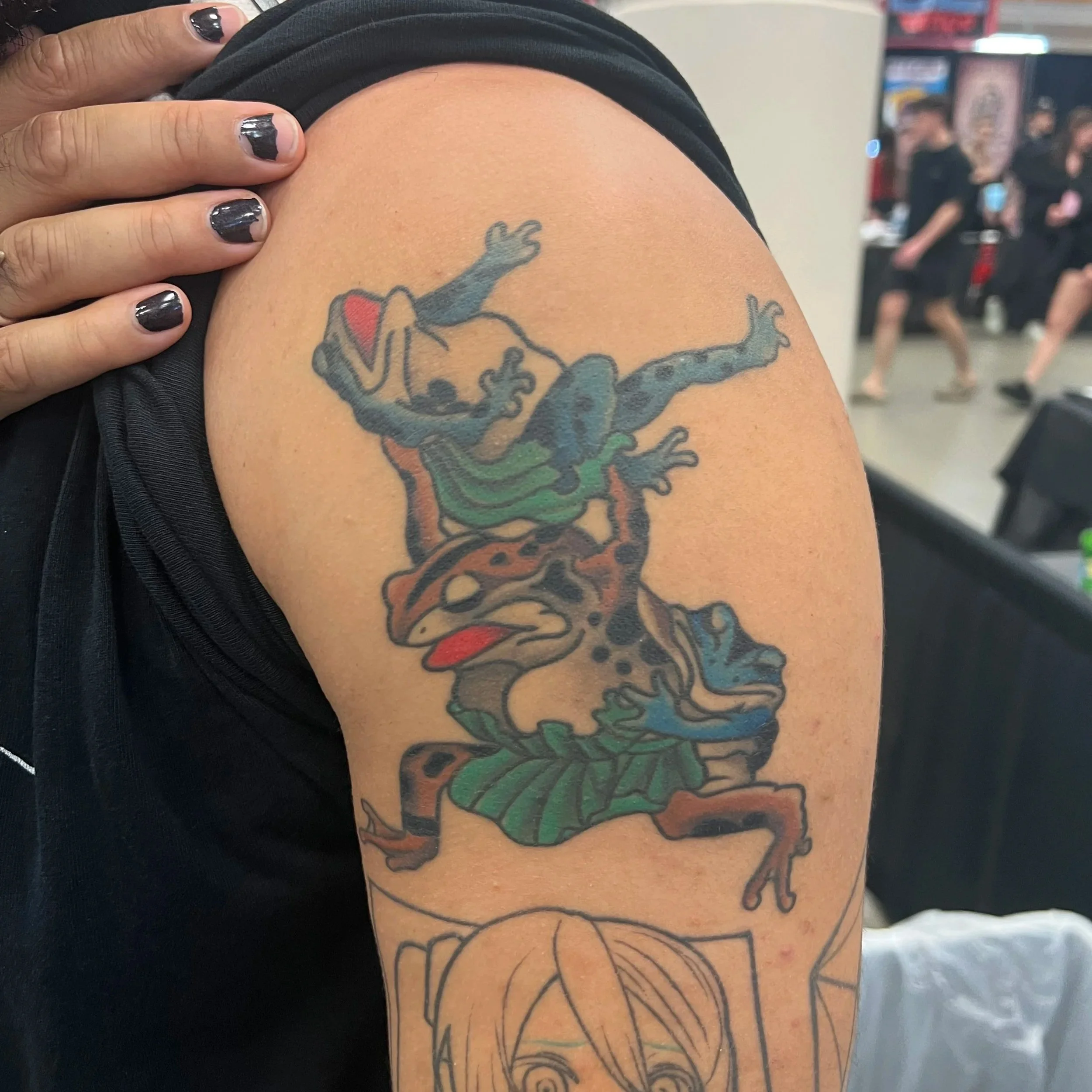 Close-up of a person's tattooed arm featuring a colorful abstract design, with a background of people in a social setting, possibly a gym or community center.