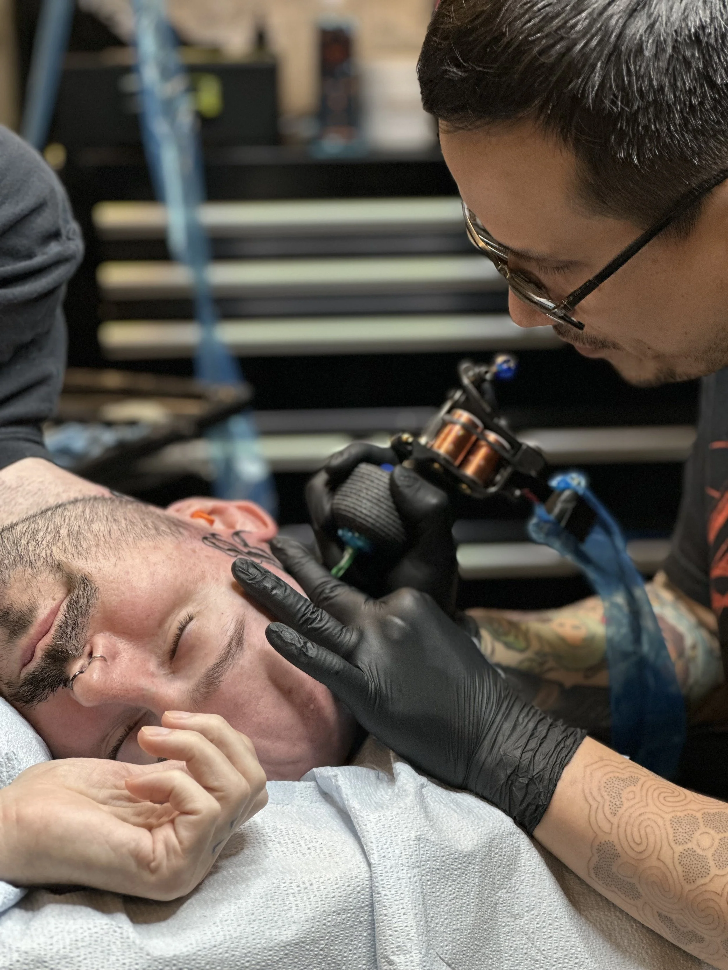 A person receives a tattoo on their face from a tattoo artist in a studio setting.