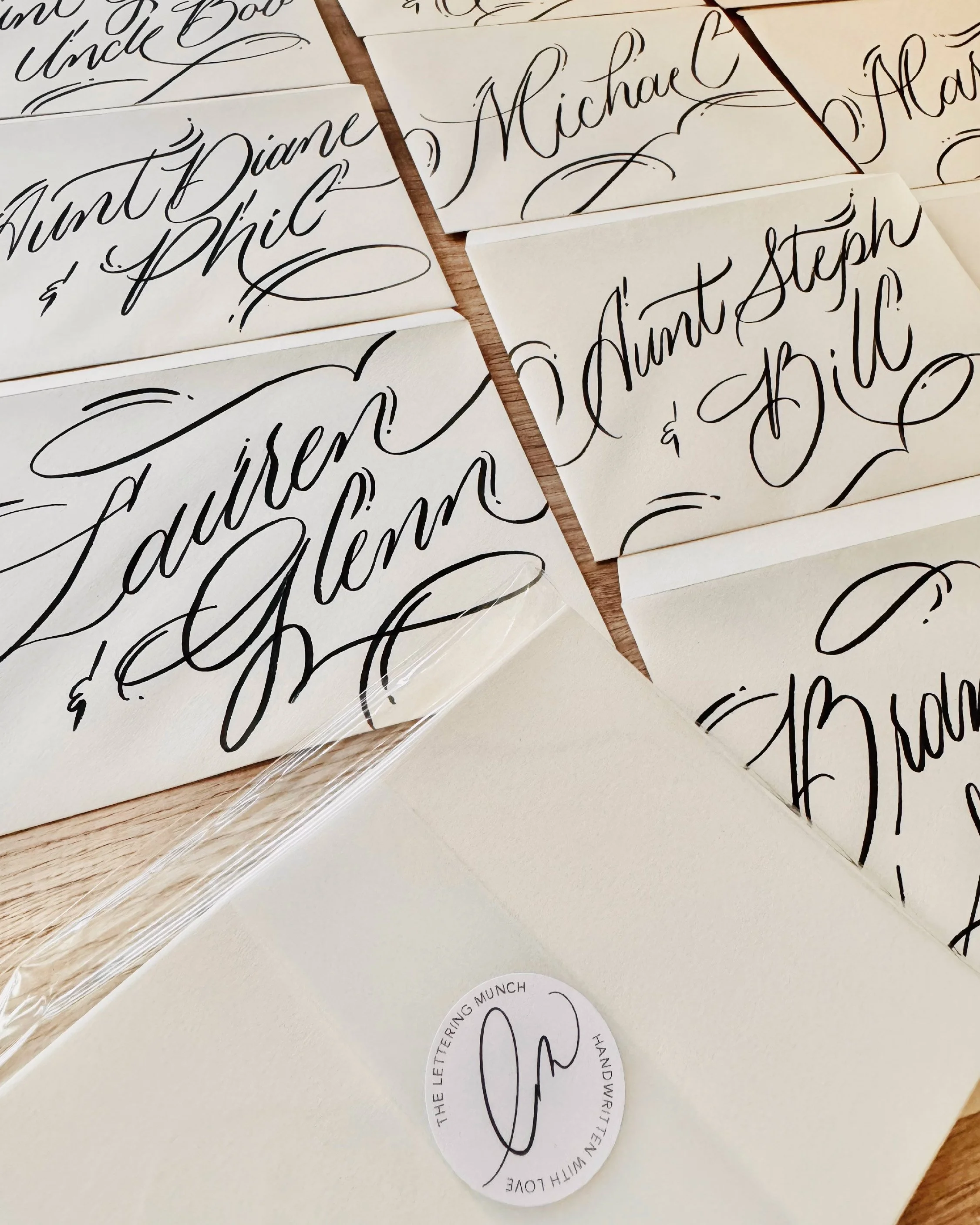 Close-up of white cards with elegant black handwritten calligraphy displaying names and decorative flourishes, wrapped in clear plastic.