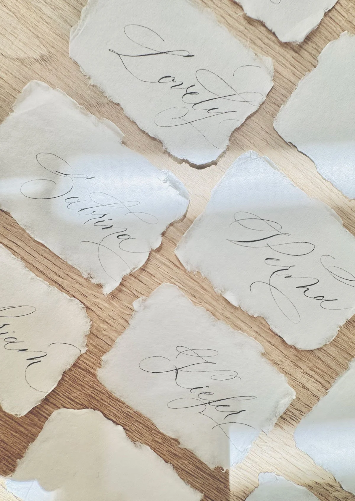 Pieces of torn paper with elegant, cursive handwriting spelling out "Wedding" on a wooden surface.