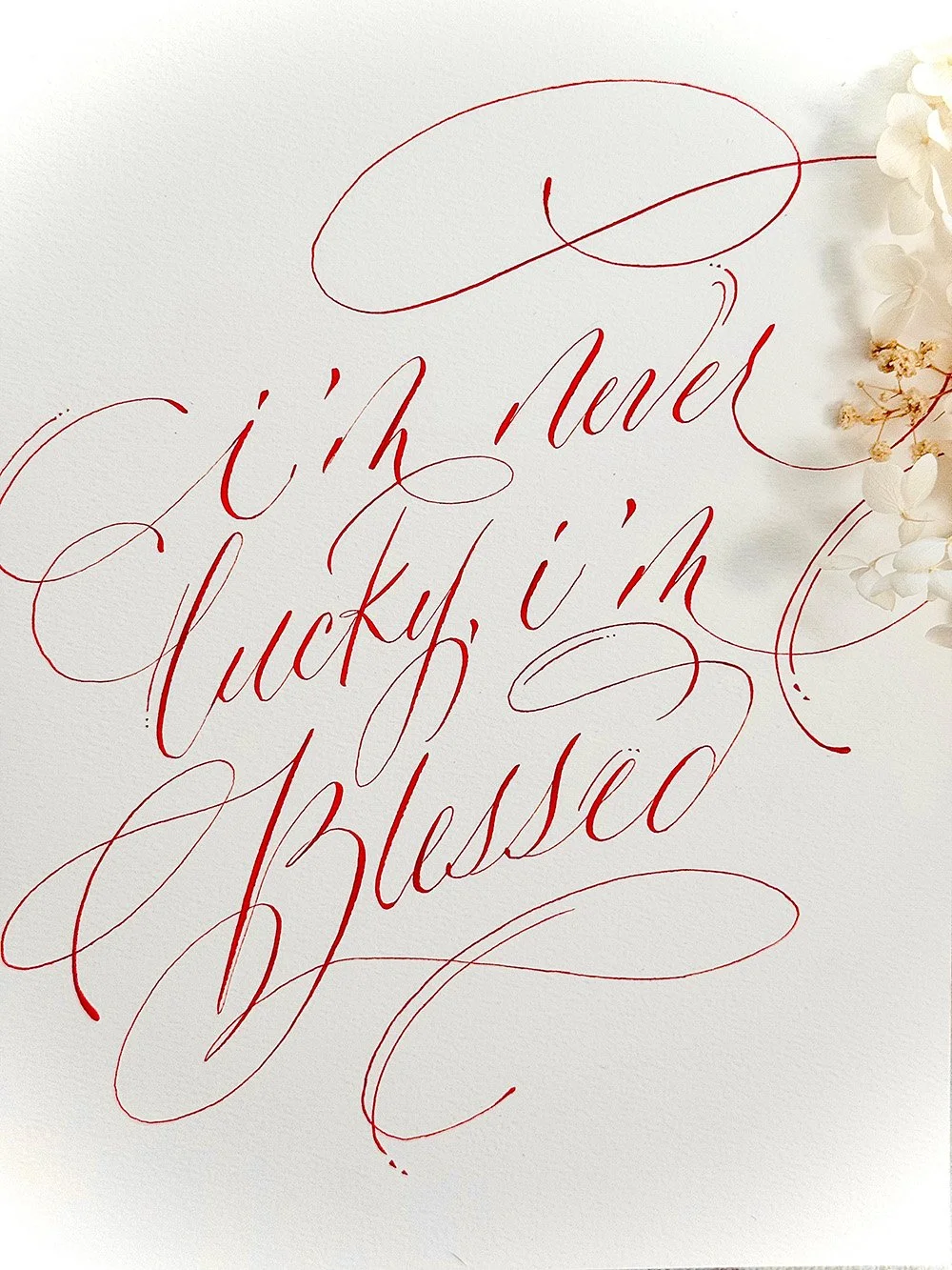 Elegant calligraphy reading "i'm lucky, i'm blessed" with white flowers on the side.