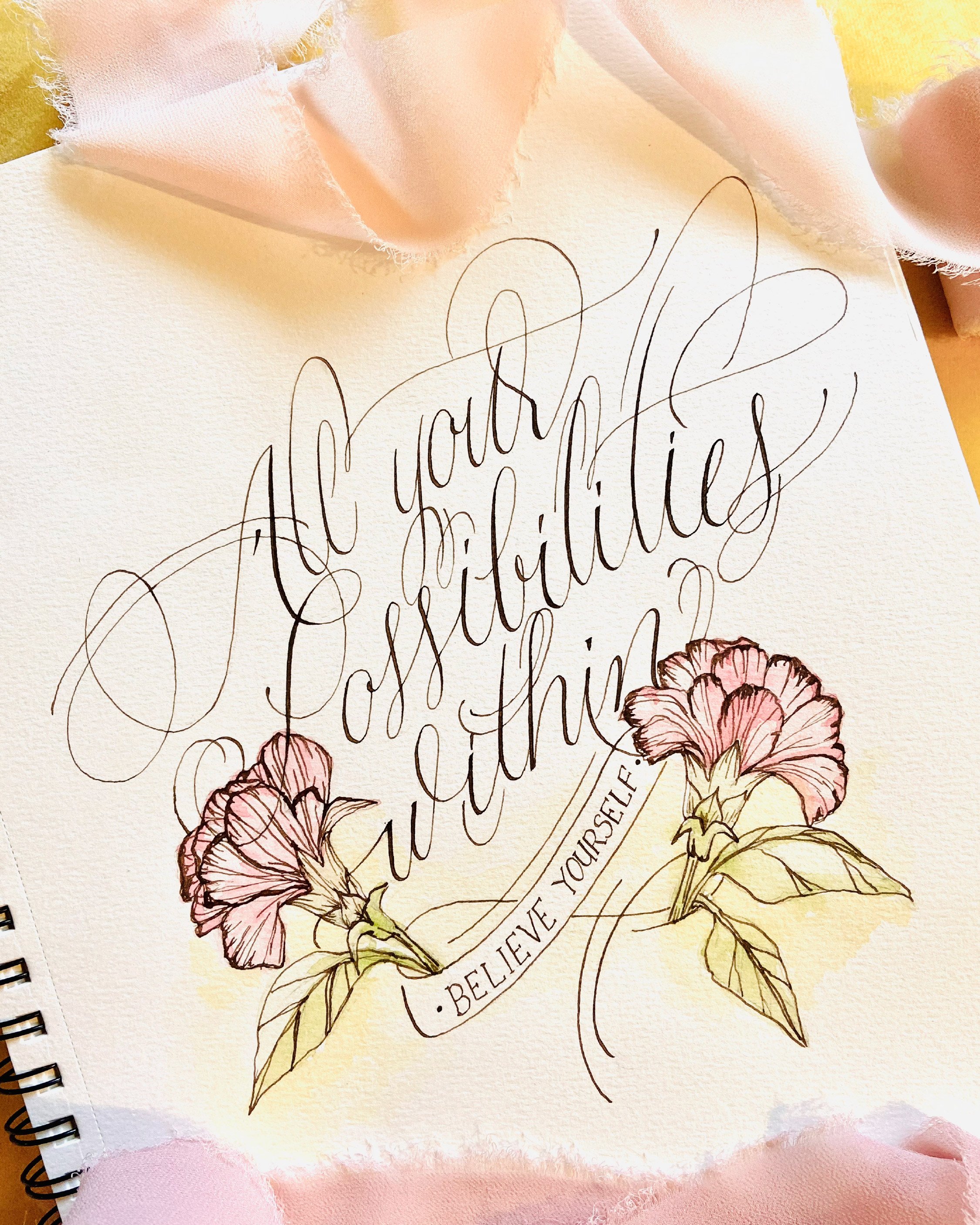 A handwritten quote on paper surrounded by pink flowers and pink tissue paper, with part of a spiral notebook visible on the left.