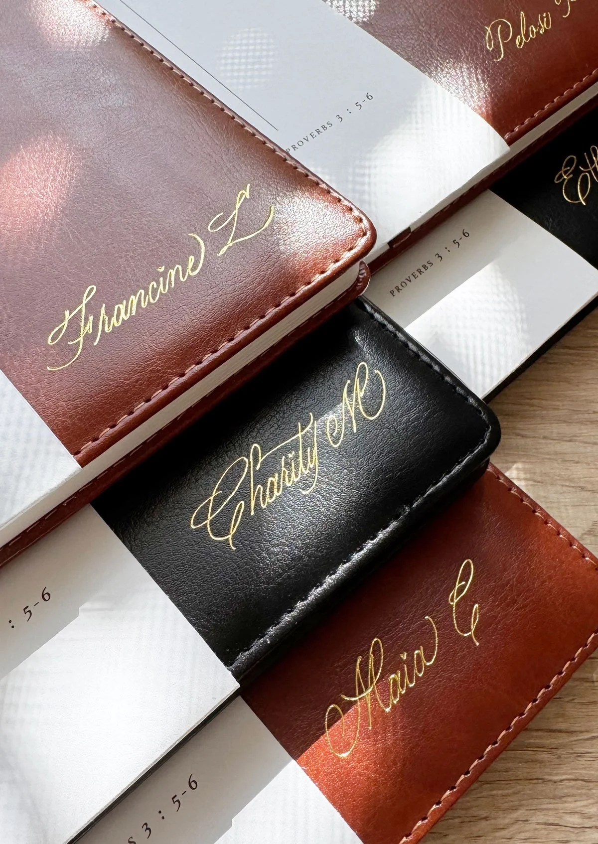 Close-up of leather-bound notebooks with titles "Finance" and "Charity" written in gold cursive lettering, overlapping on paper with Bible verse references.