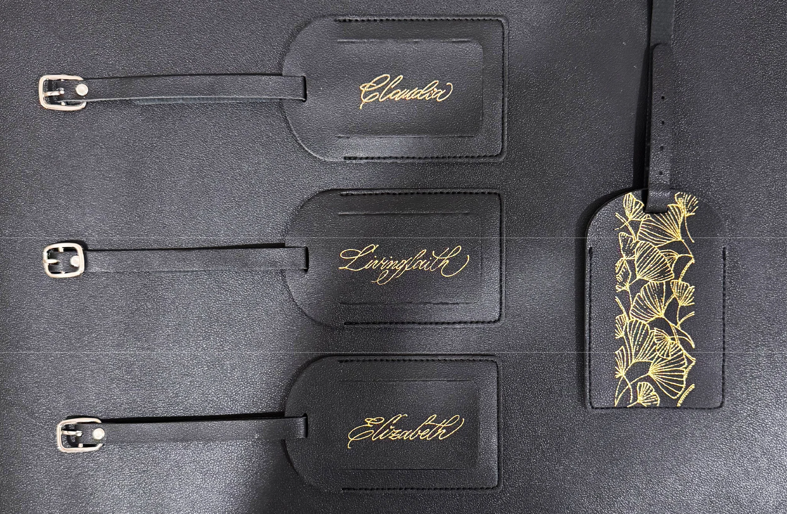 Close-up of black leather accessories, each with a gold signature or floral design, including names like 'Claudia,' 'Livingfaith,' and 'Elizabeth,' with buckles attached.