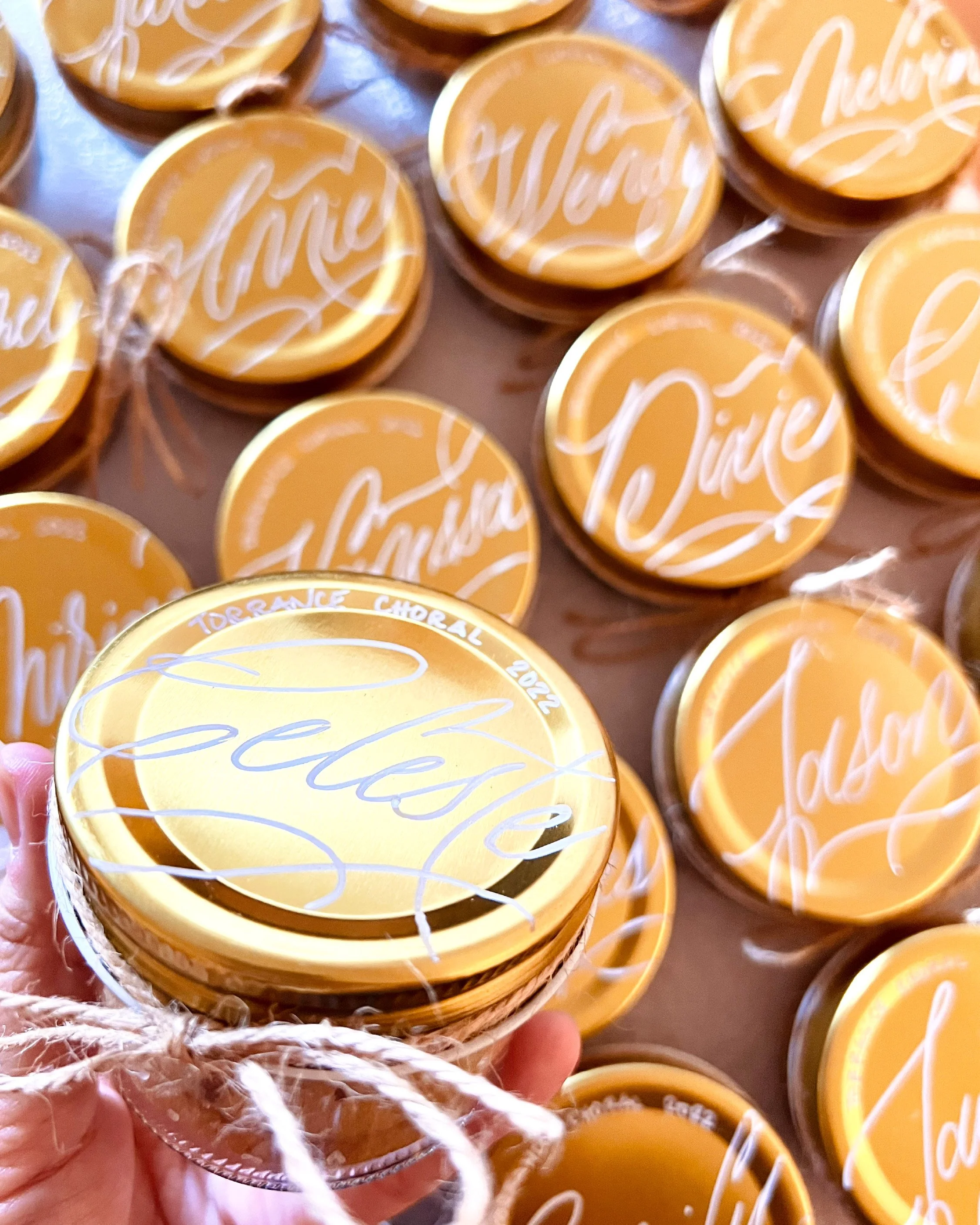 Yellow buttons with white cursive writing that says 'Chérie,' held in hand with a woven basket containing similar buttons in the background.