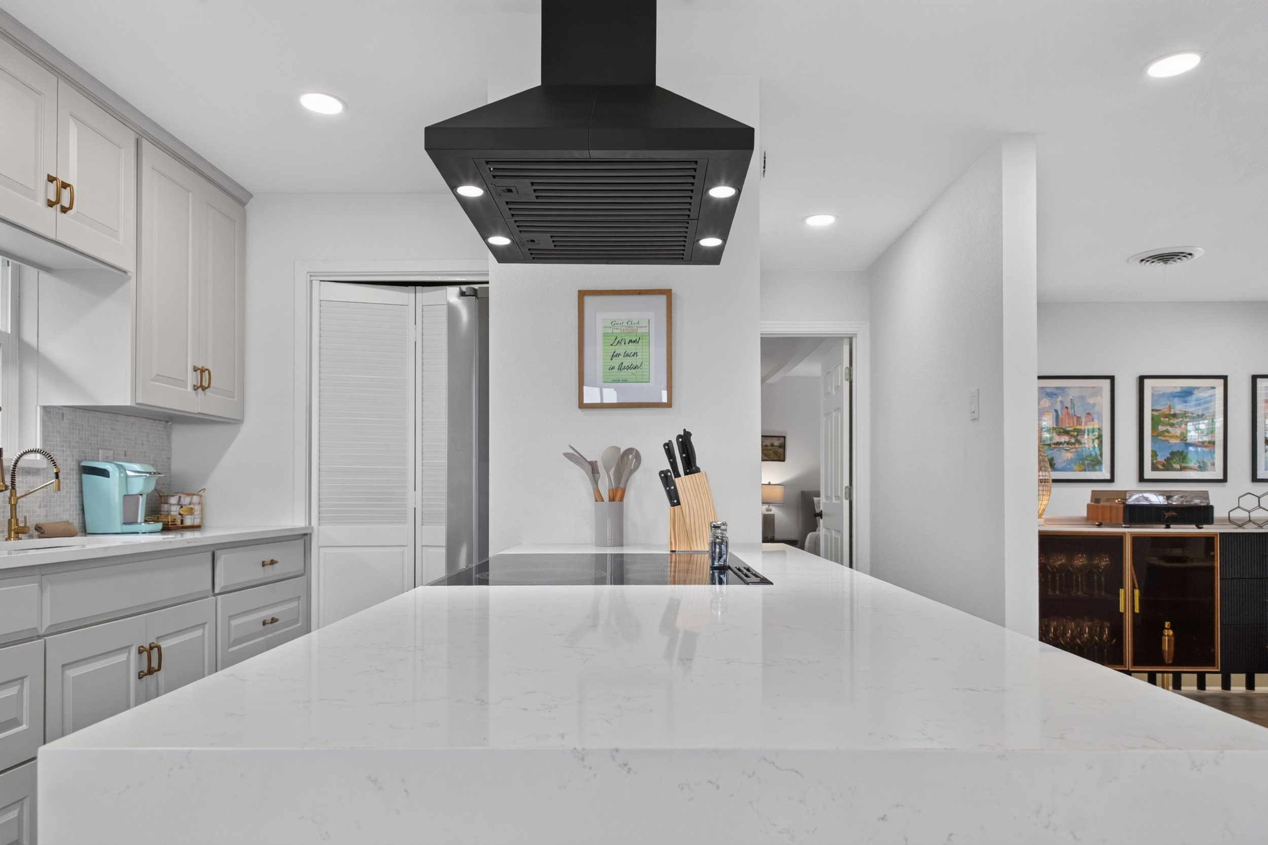 Modern kitchen with white cabinetry, a white island, black range hood, and artwork on the walls.