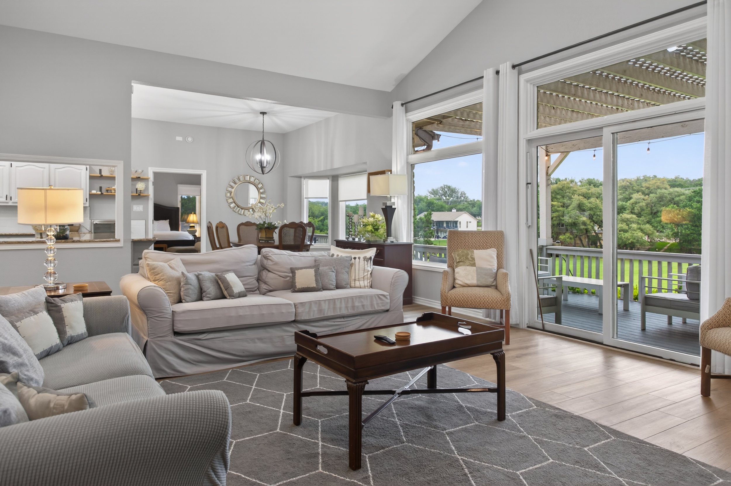 Living room with beige sofas, a wooden coffee table, and large windows showing an outdoor deck and greenery.