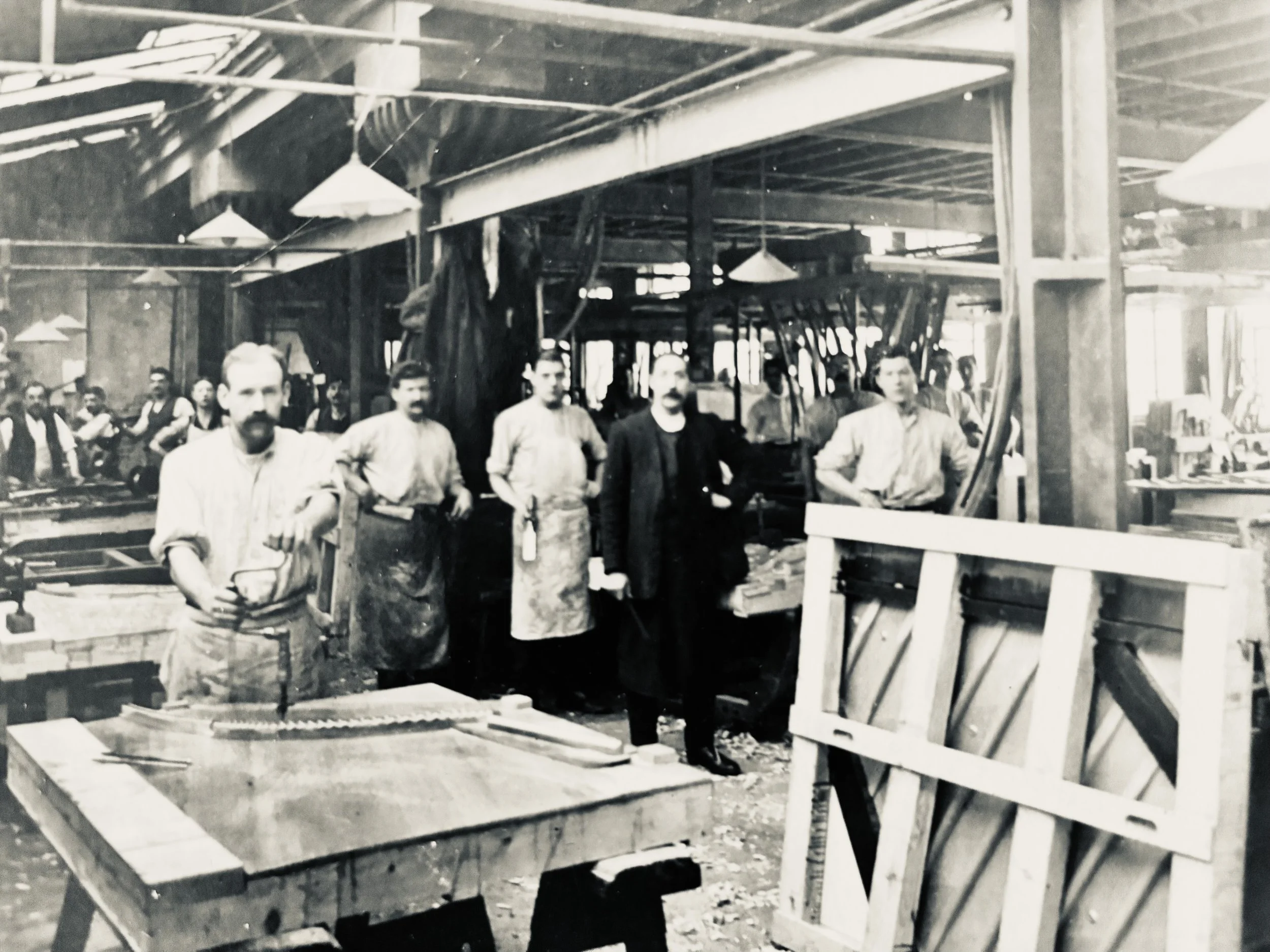 Black and white photo of workers on a construction site, standing among wooden structures and tools.