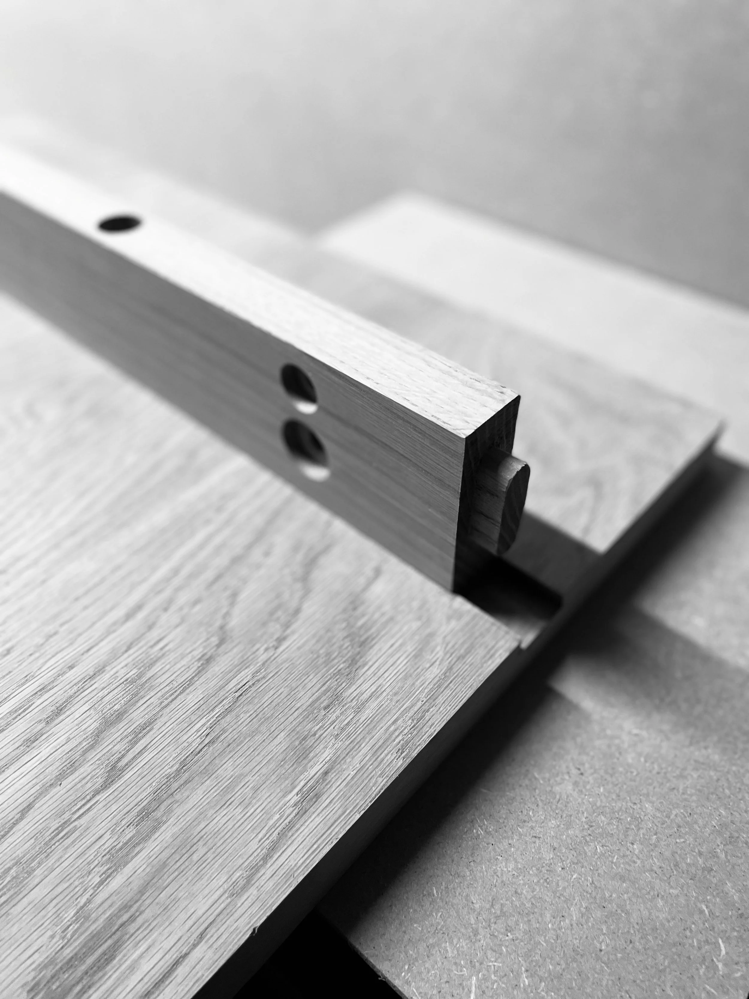 Close-up photograph of a metallic square tube with holes, placed on a wooden surface.