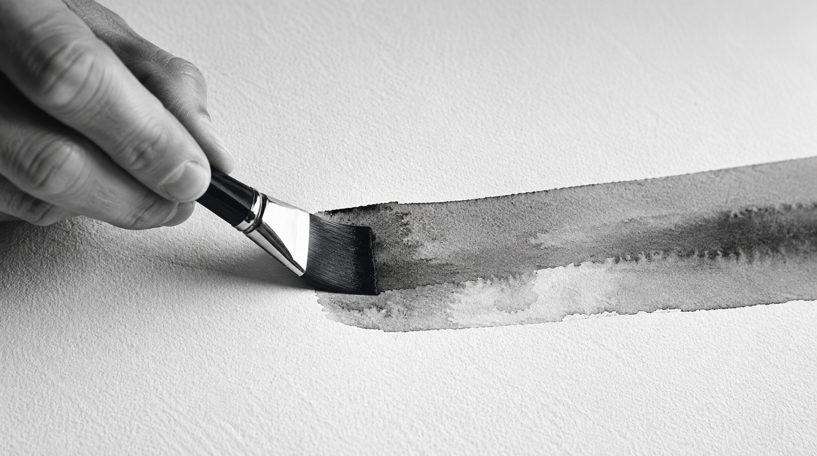 Close-up of a hand wearing a glove applying black watercolor paint with a brush on textured white paper.