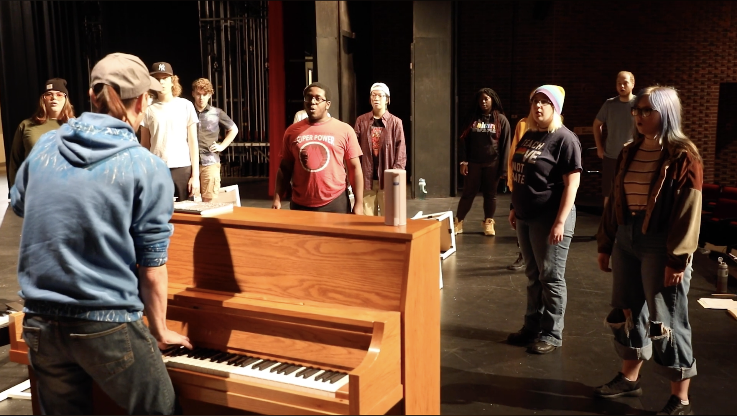 People standing and singing behind a piano.
