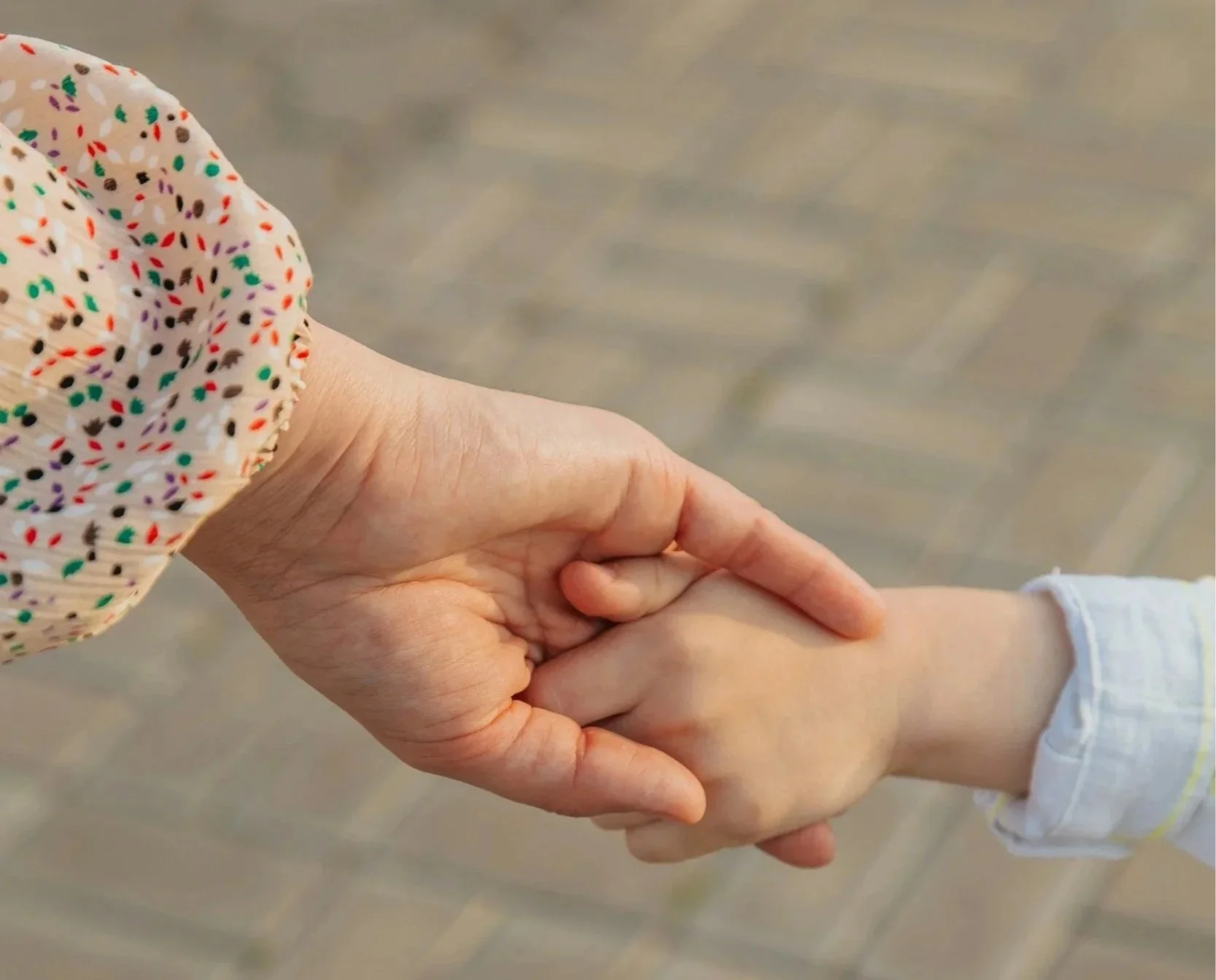 A person with a colorful, polka-dotted sleeve gently holding someone else's wrist in a comforting manner.