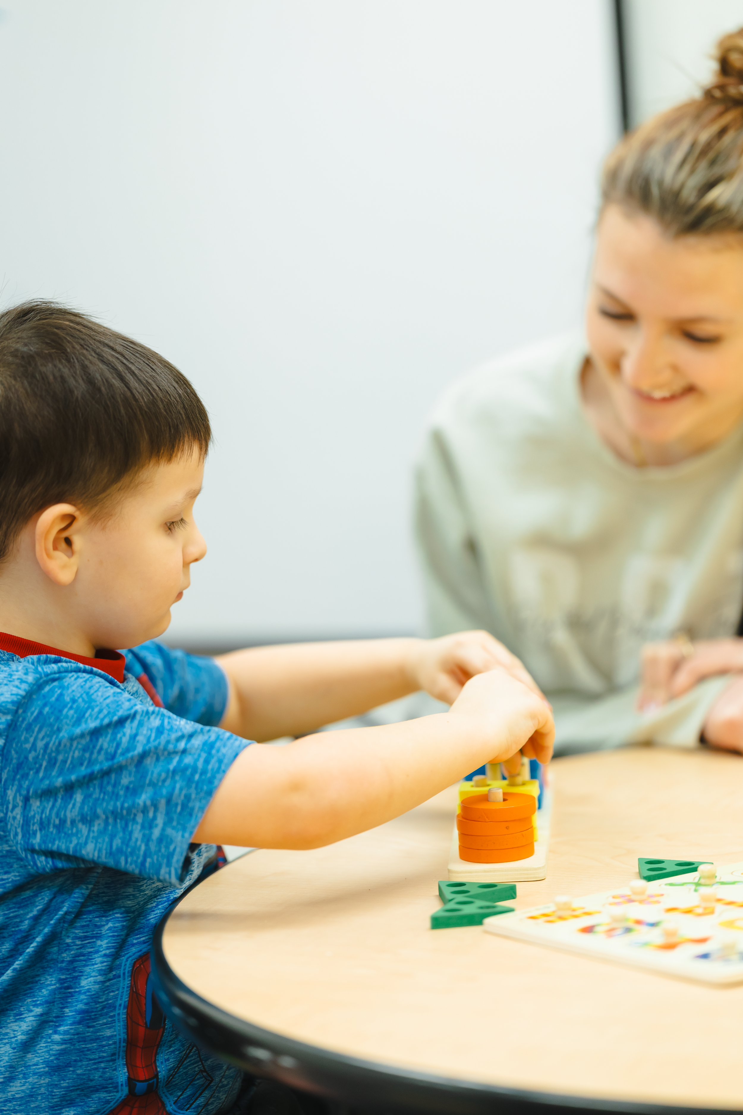 A young boy and a woman sitting at a table playing a board game with colorful tiles and game pieces.