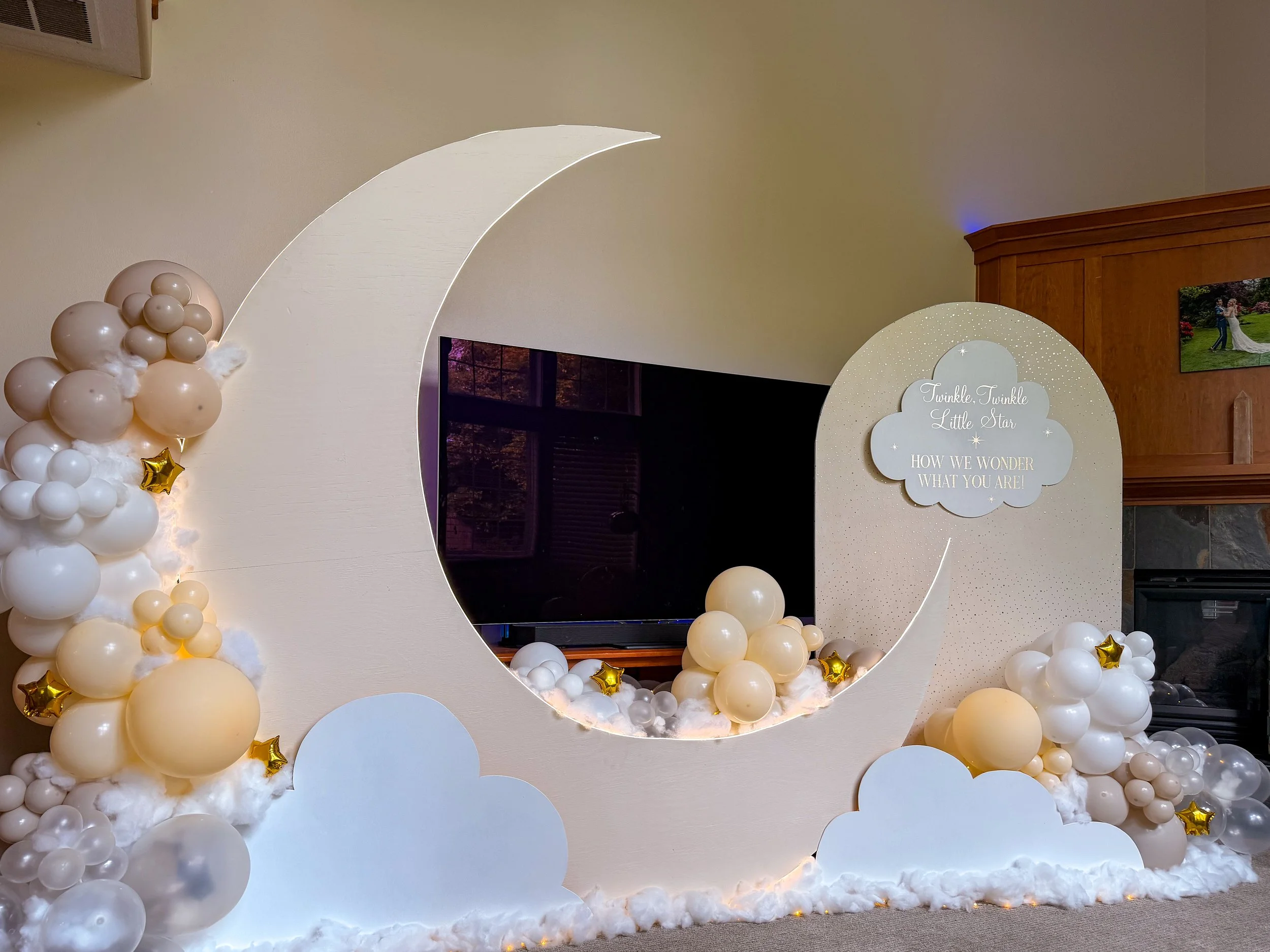 Baby shower backdrop with a large white crescent moon, clouds, balloons, gold stars, and a sign reading “Twinkle, Twinkle Little Star.”
