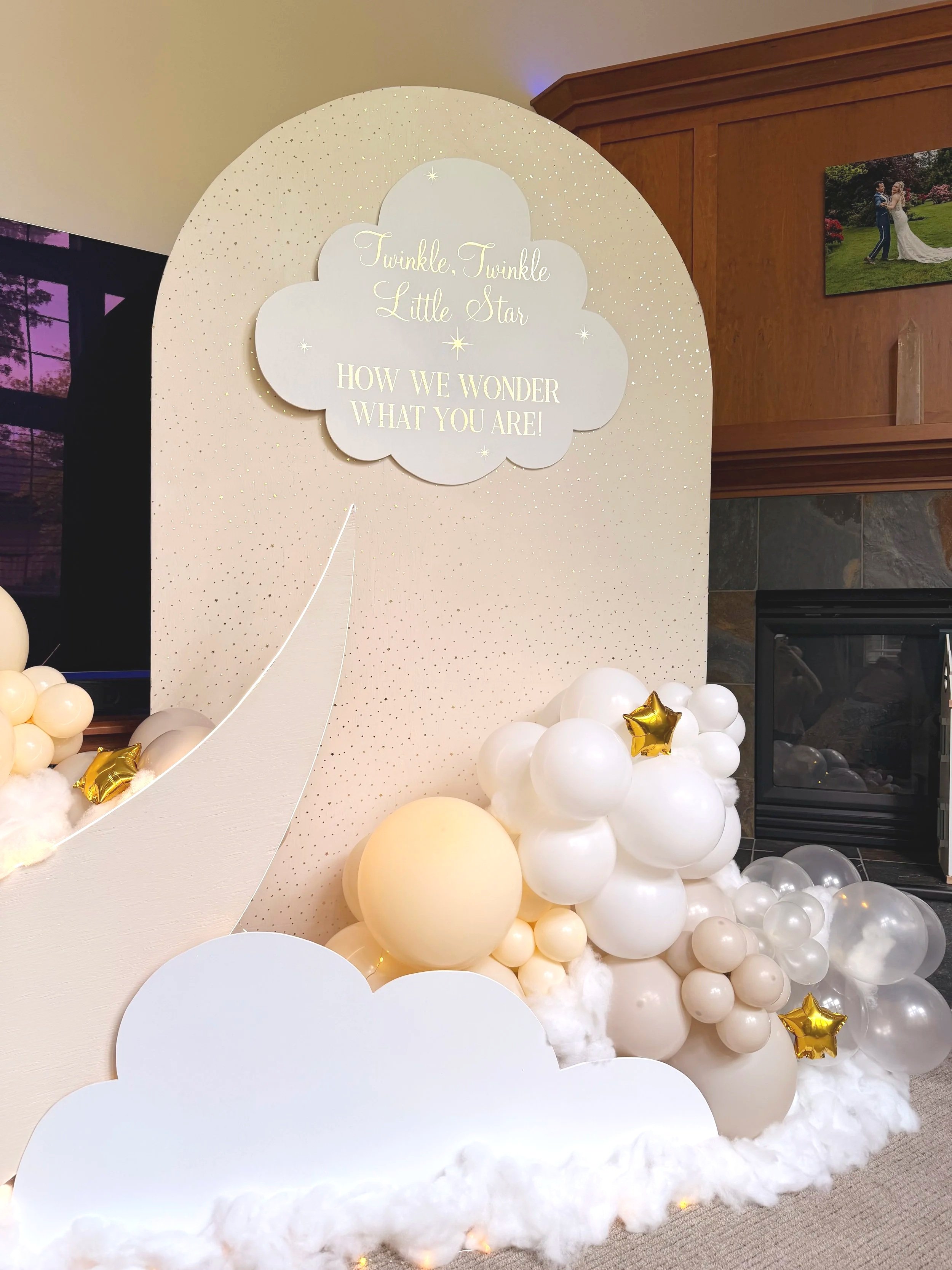 Celestial baby shower or nursery decor with a starry backdrop, cloud-shaped sign reading “Twinkle, Twinkle Little Star,” white and gold balloon garland, and crescent moon.