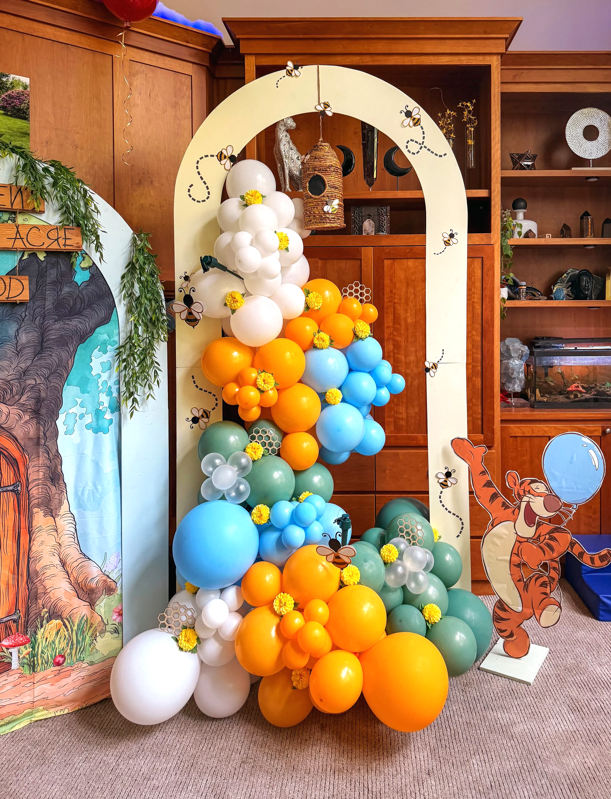Colorful Winnie-the-Pooh-themed balloon arch with bee decorations, honeycomb accents, and a beehive centerpiece.