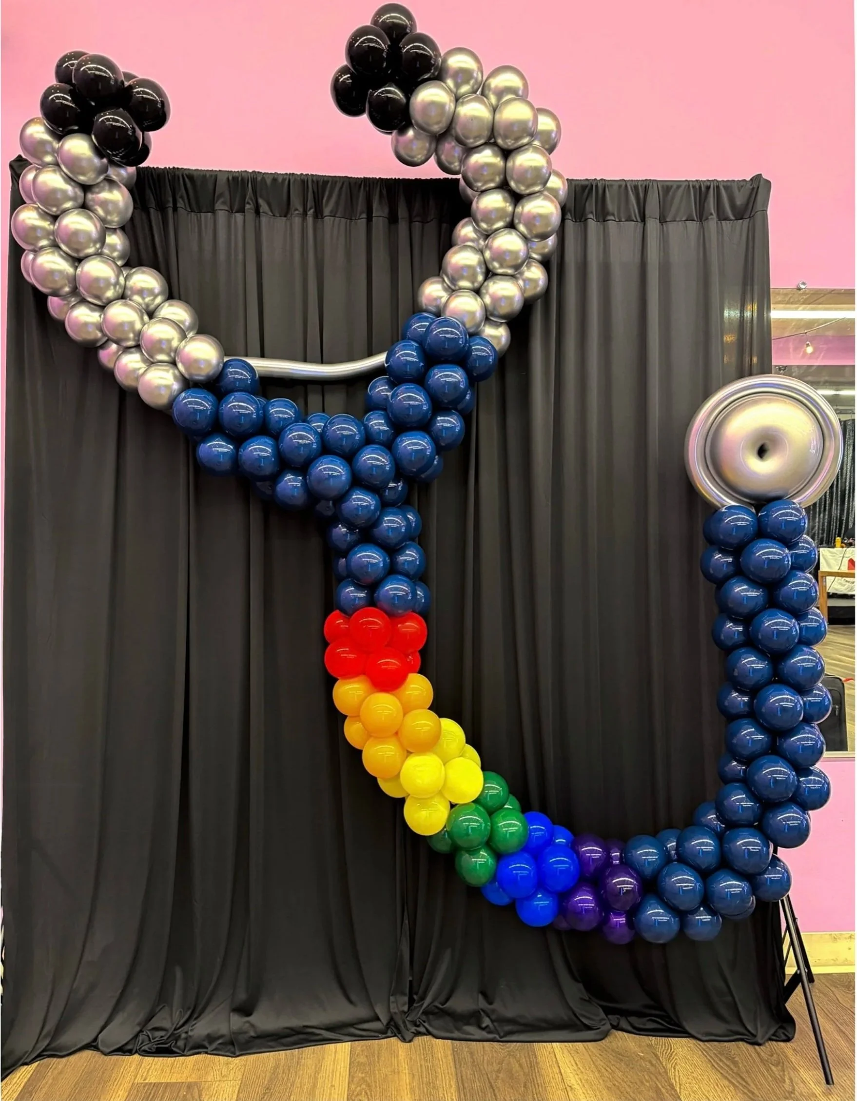 Colorful balloon sculpture resembling a stethoscope against a black backdrop, with rainbow tubing and silver accents.