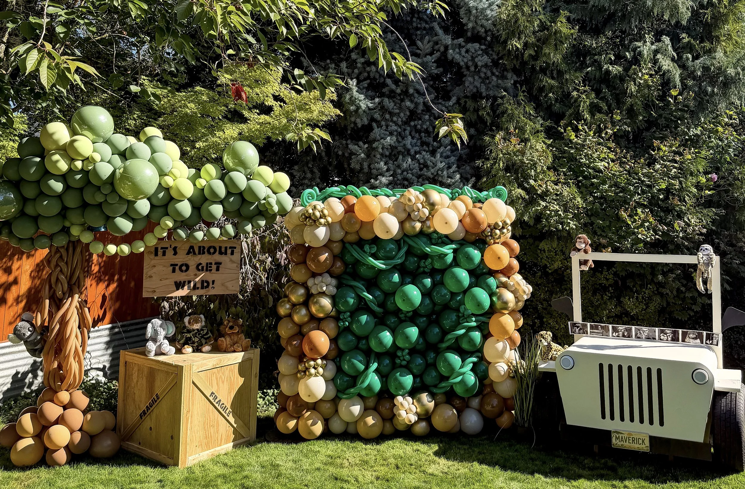 Colorful balloon jungle-themed display featuring a green-and-orange balloon monkey, balloon crocodile, jungle foliage, crates, and a small white safari vehicle.