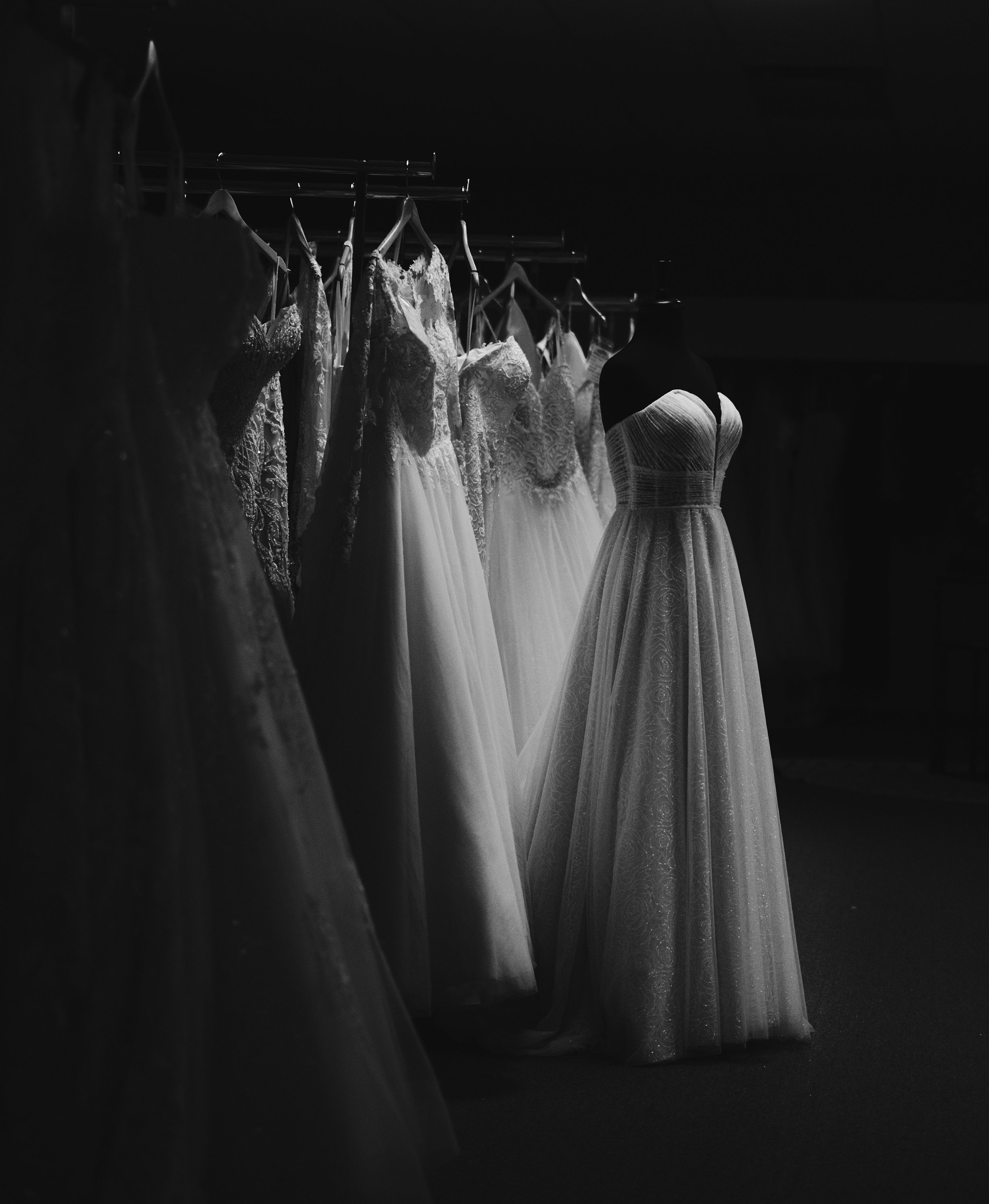 Black and white photo of wedding dresses hanging on a rack, displayed on mannequins.