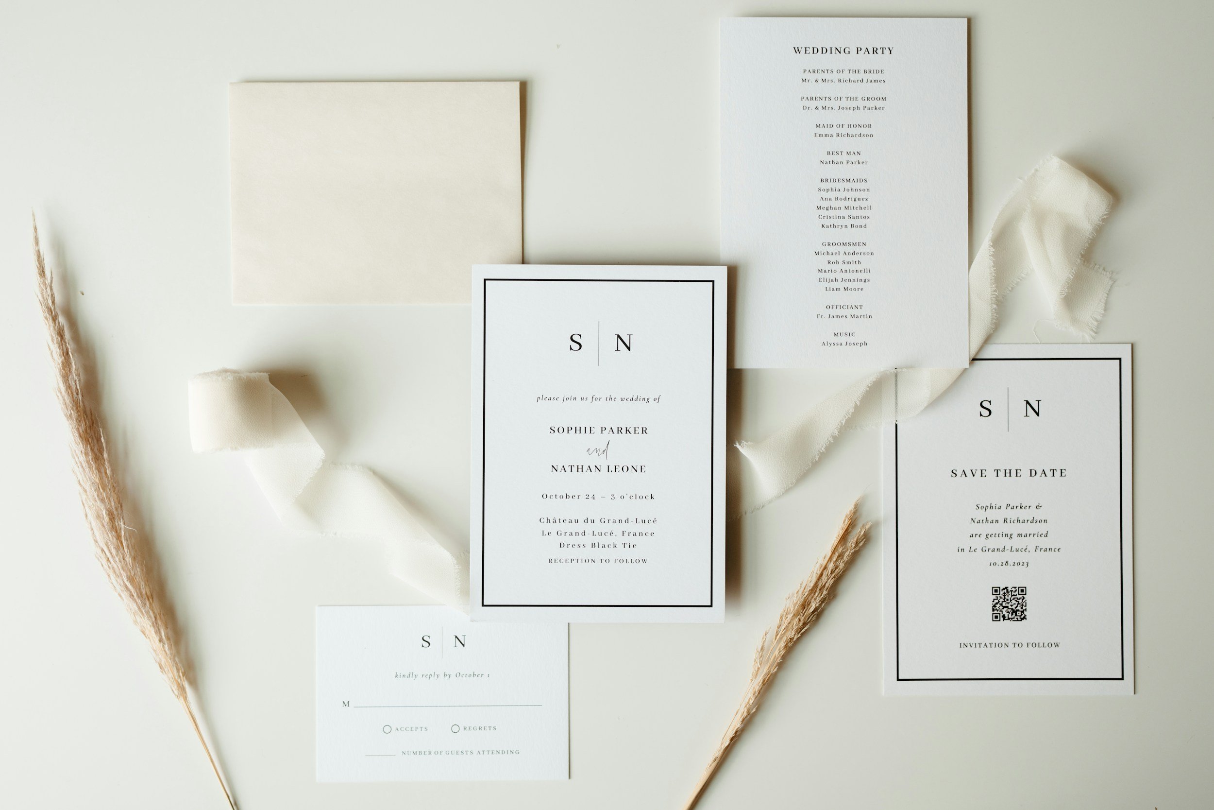 Wedding invitations and RSVP cards arranged on a white surface with beige decorative grasses and fabric accents.