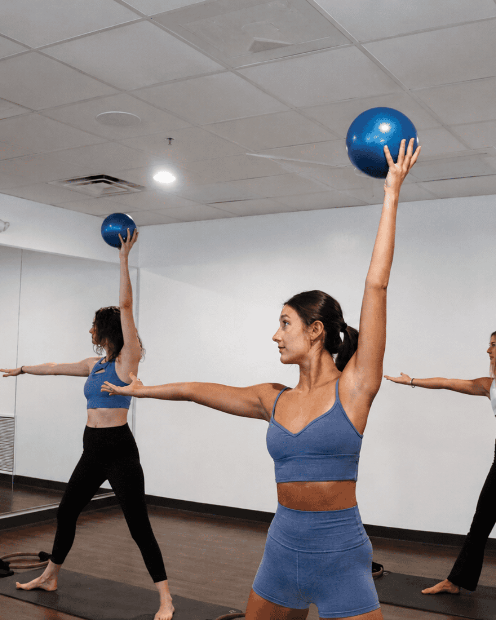 People participating in a barre class using blue exercise balls at yoga pod tucson.